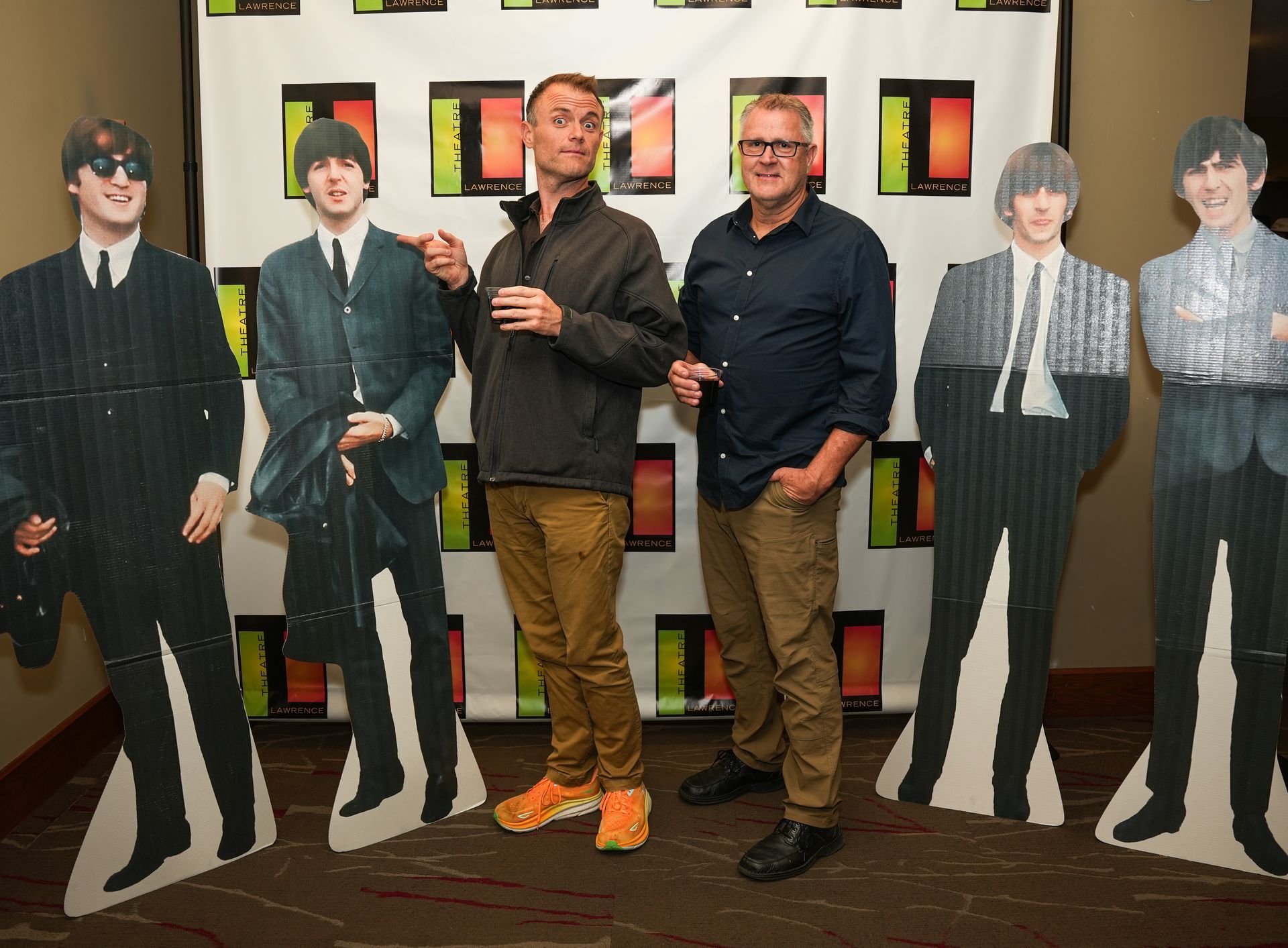 Two men pose with Beatles cardboard cutouts at an event. They are pointing and smiling.