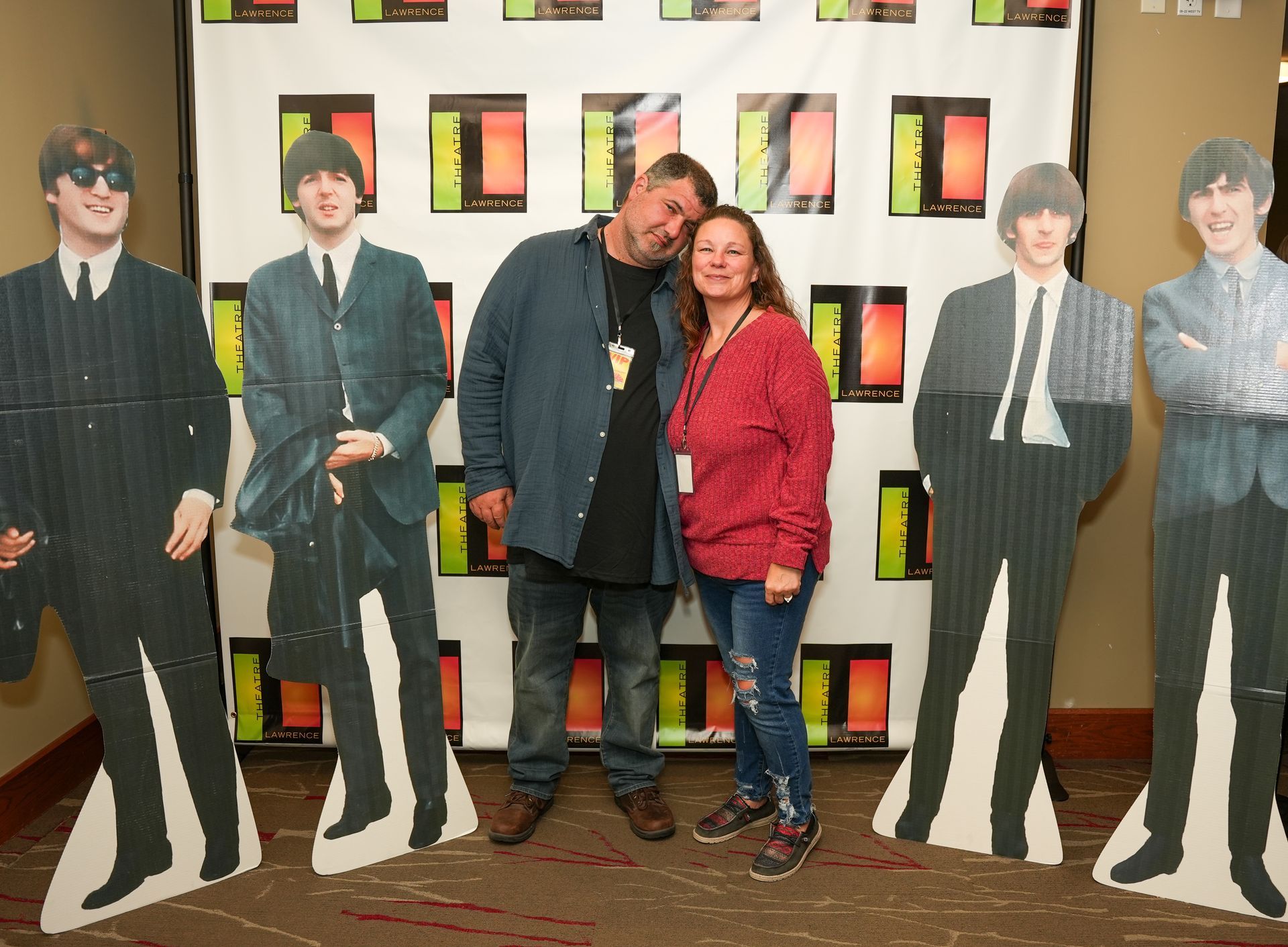 A couple poses with Beatles standees in front of a backdrop.
