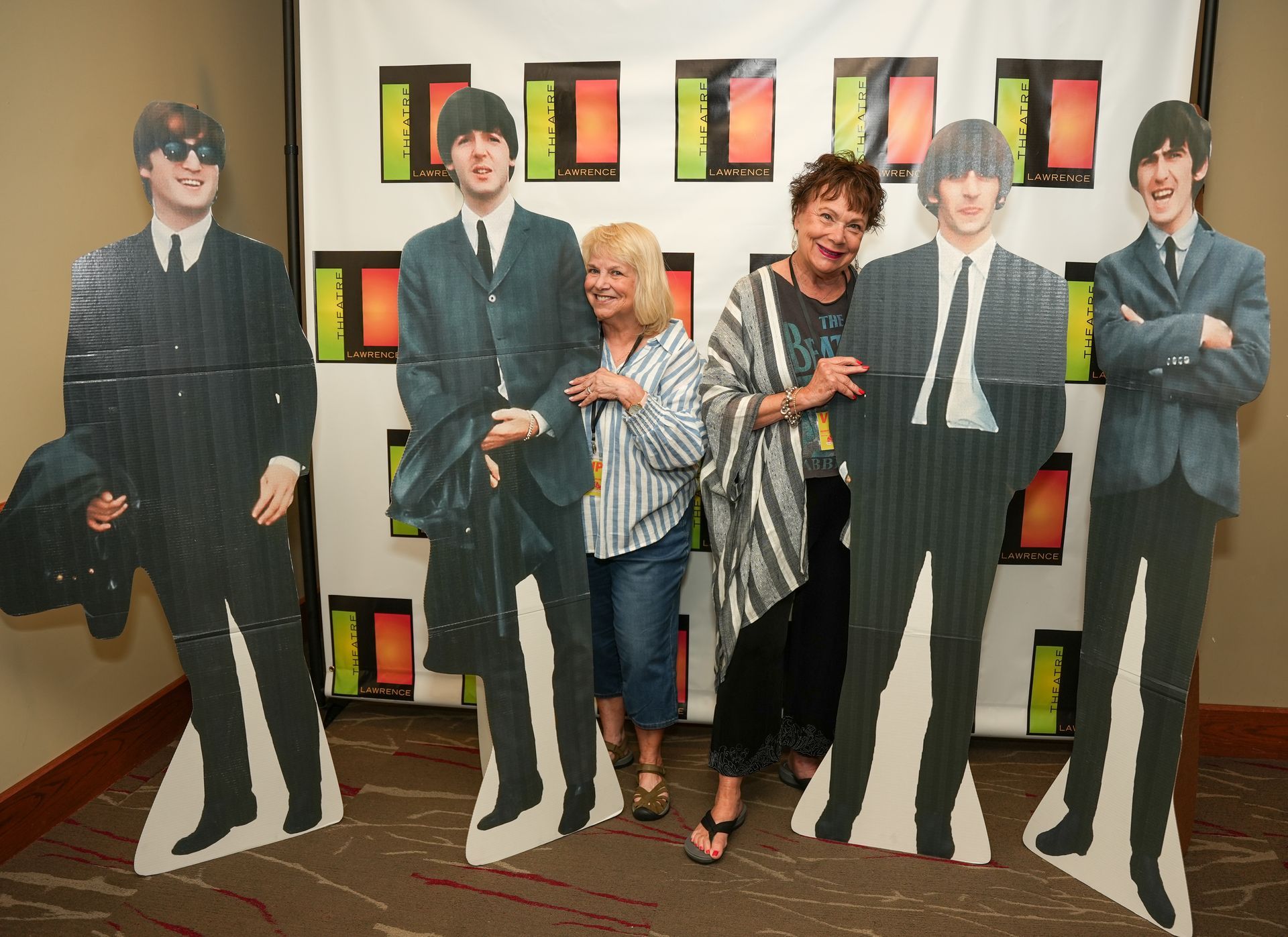 Two women pose with cardboard cutouts of The Beatles. White backdrop.
