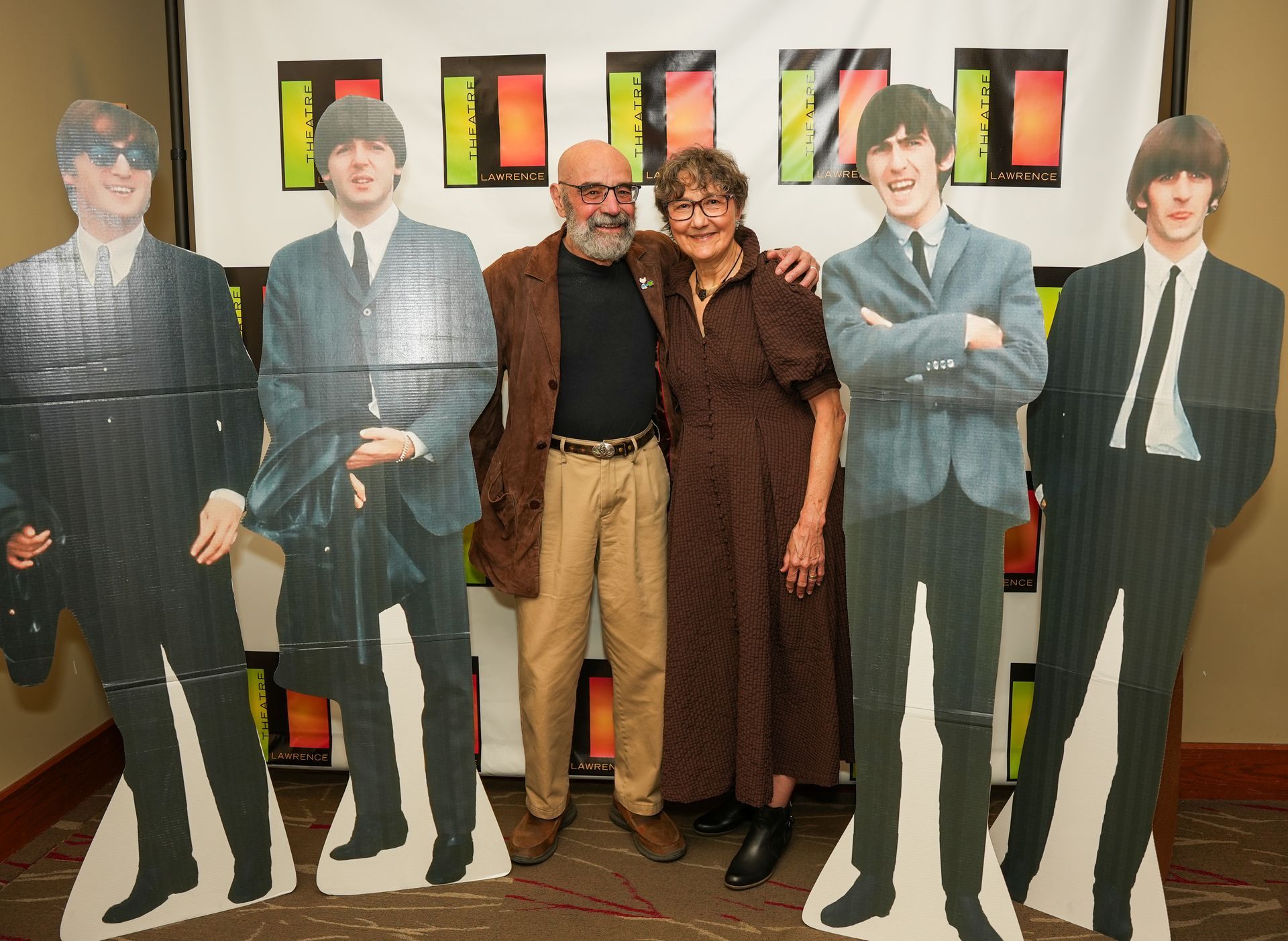 Couple poses with Beatles cutouts; event backdrop with colorful rectangles.
