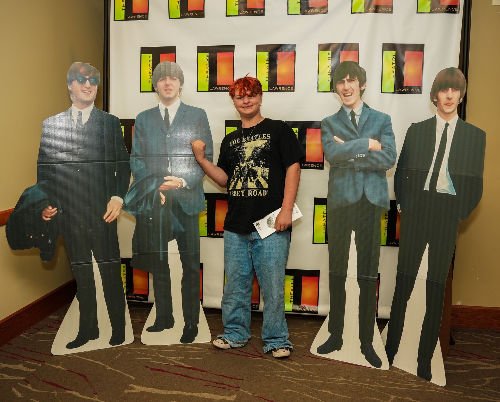 Person posing with Beatles cardboard cutouts at an event.