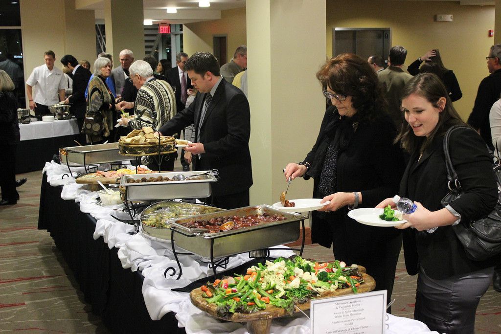 People at a buffet, selecting food. The setting is an event space with various dishes and attendees.