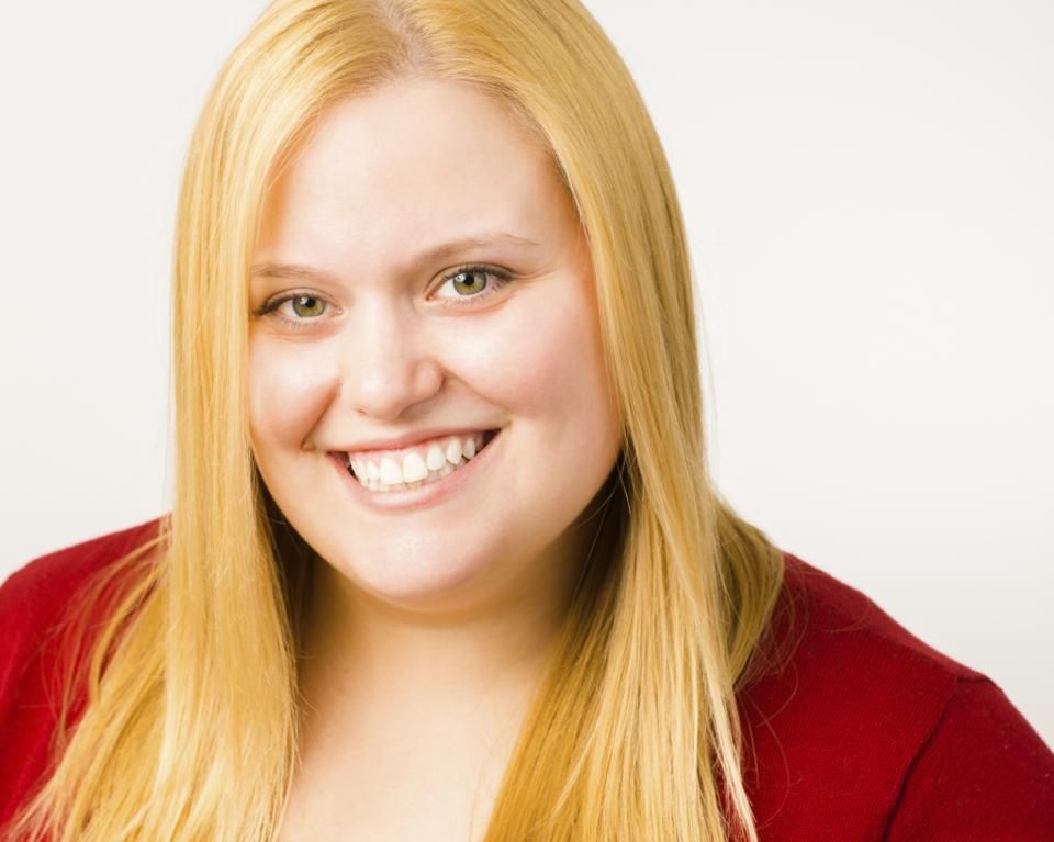 A woman with long blonde hair is smiling and wearing a red shirt.