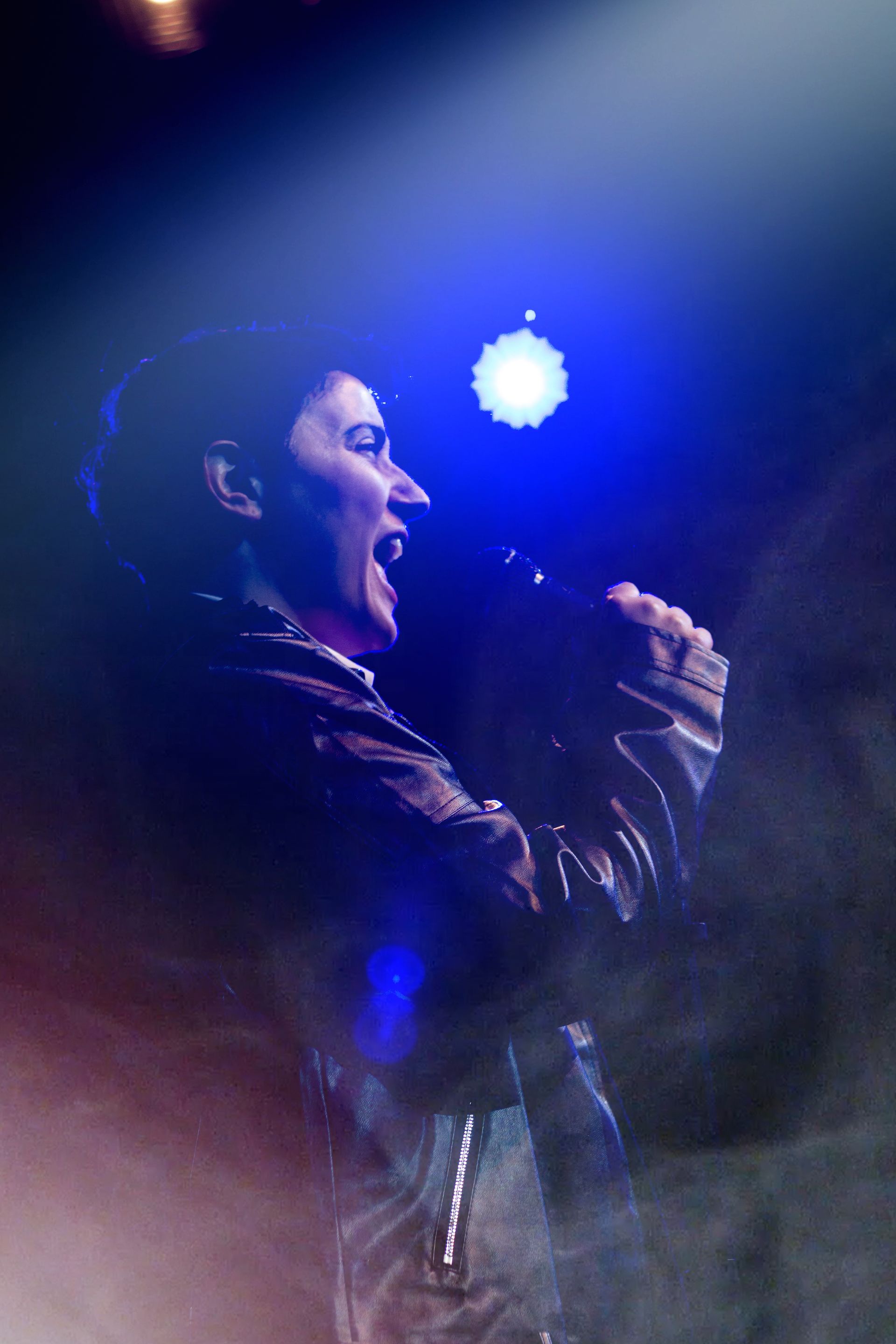 Woman singing passionately into a microphone, lit by blue stage lights in a smoky environment.