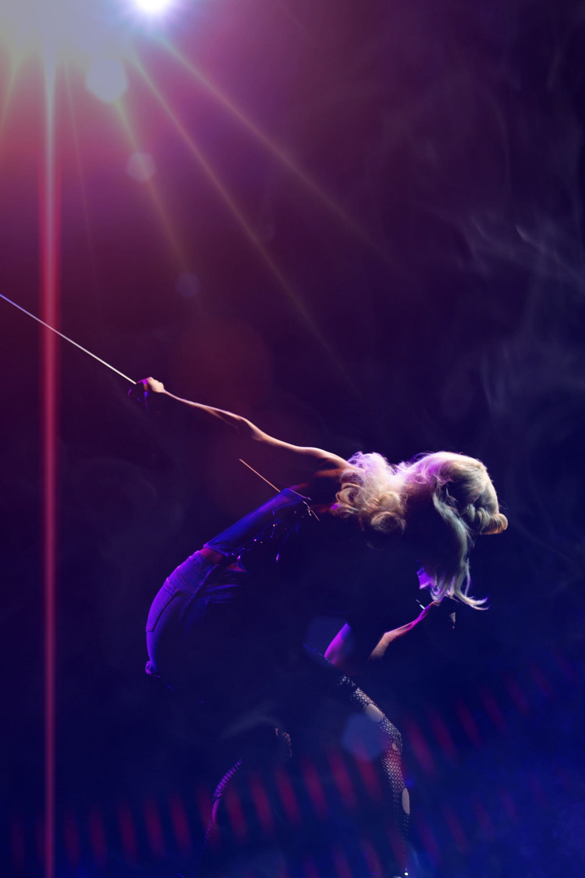 A performer in silhouette against a bright spotlight. They are holding a rope and leaning forward,