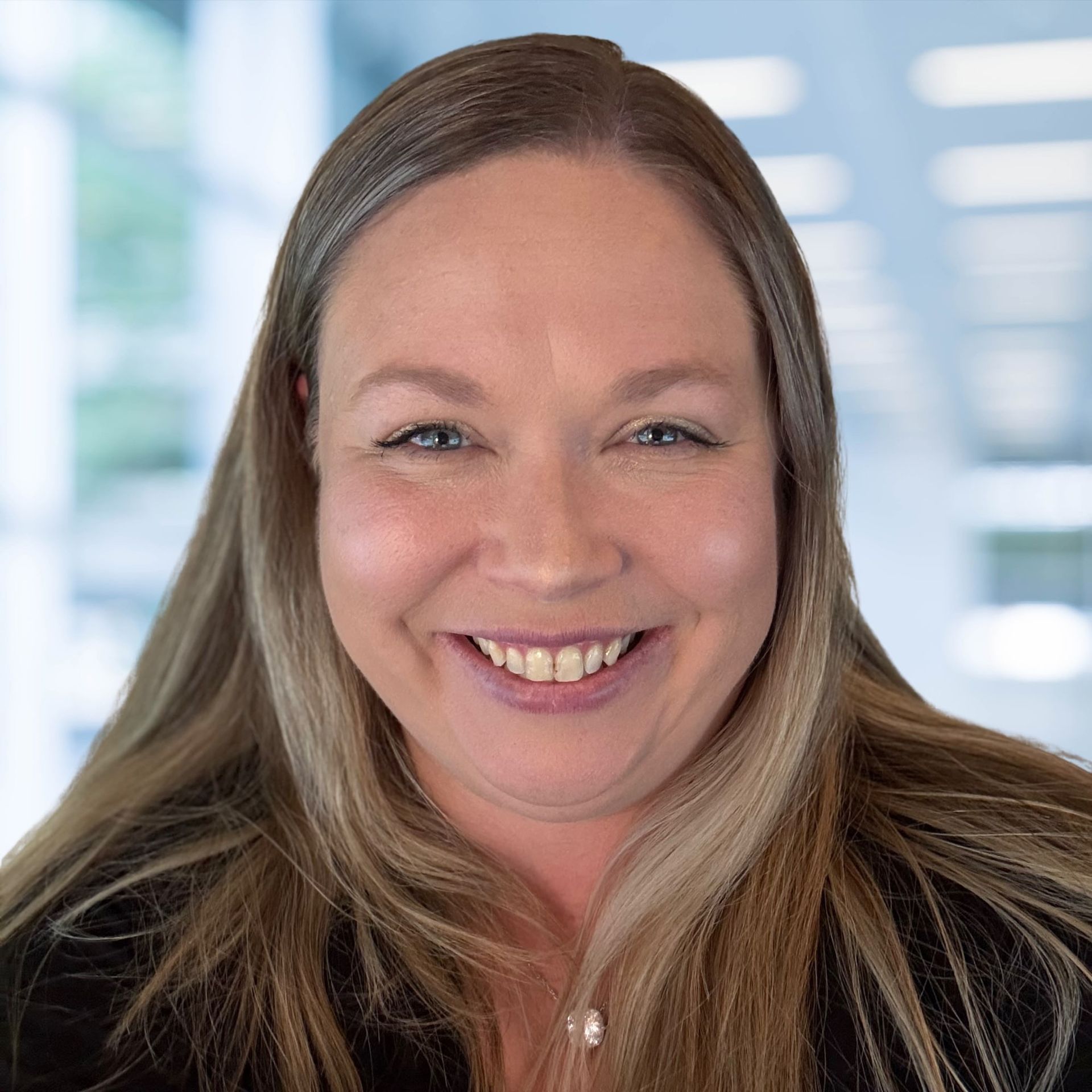 Woman with light brown hair smiles at the camera, indoors.