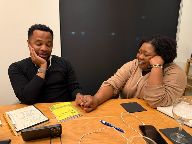 Couple at a table, holding hands. Man looks pensive, woman smiles.