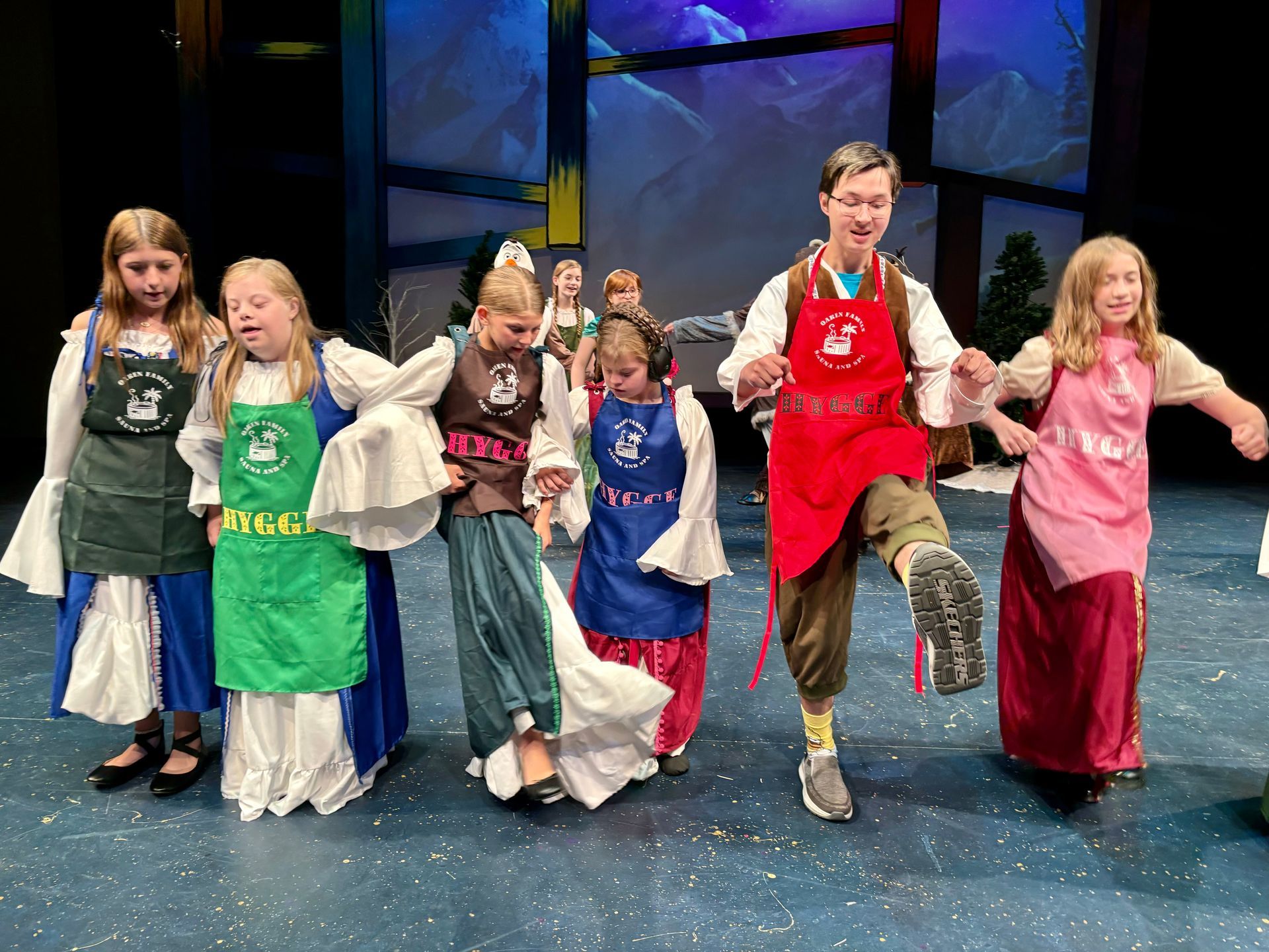 A group of children in aprons are dancing on a stage.