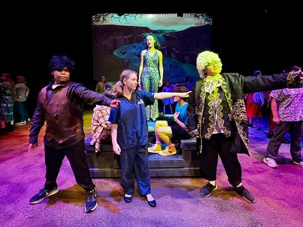 Actors on stage in colorful costumes, performing in a play with a scenic backdrop of a canyon.