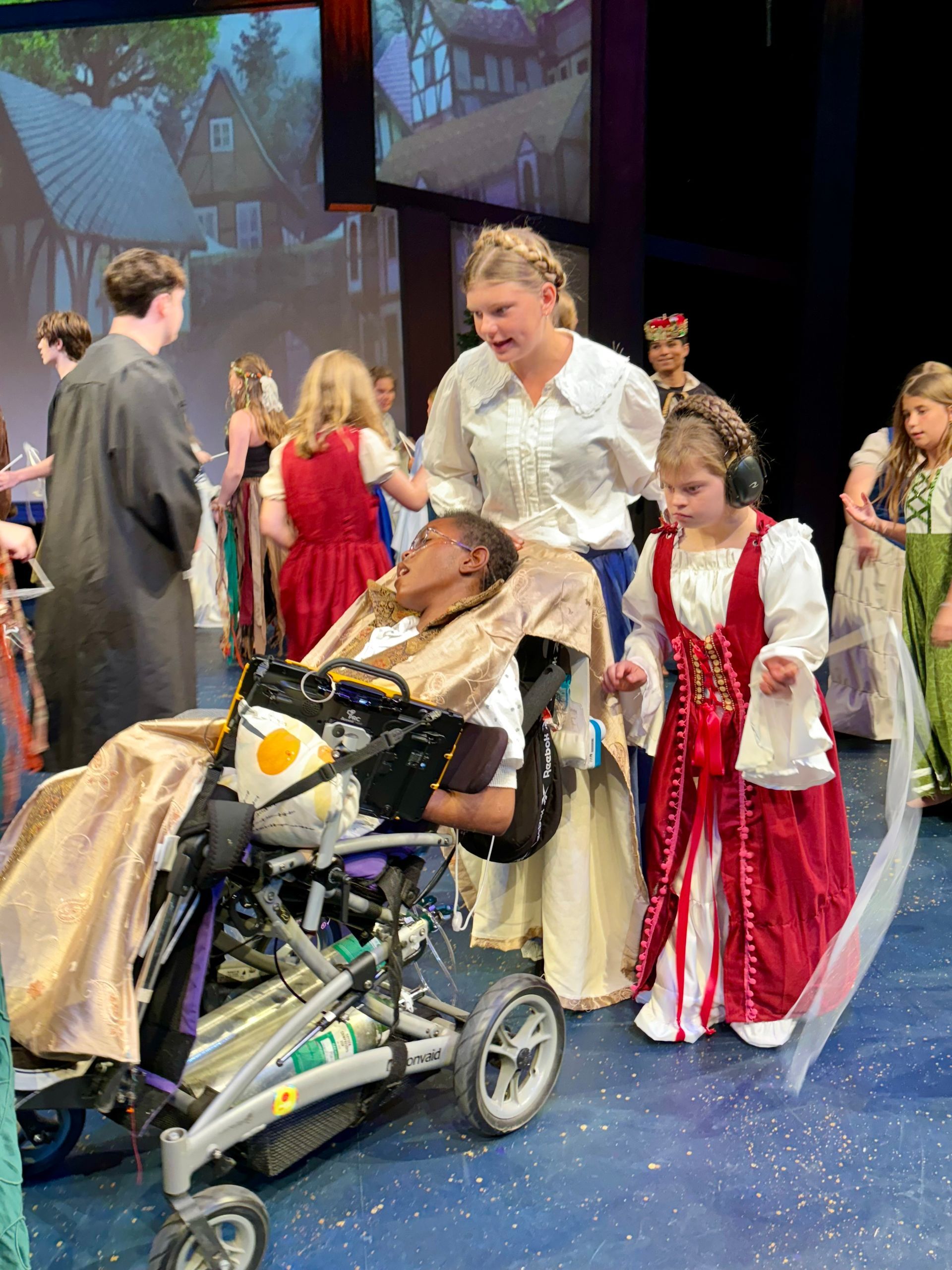 A group of people are standing around a man in a wheelchair on a stage.