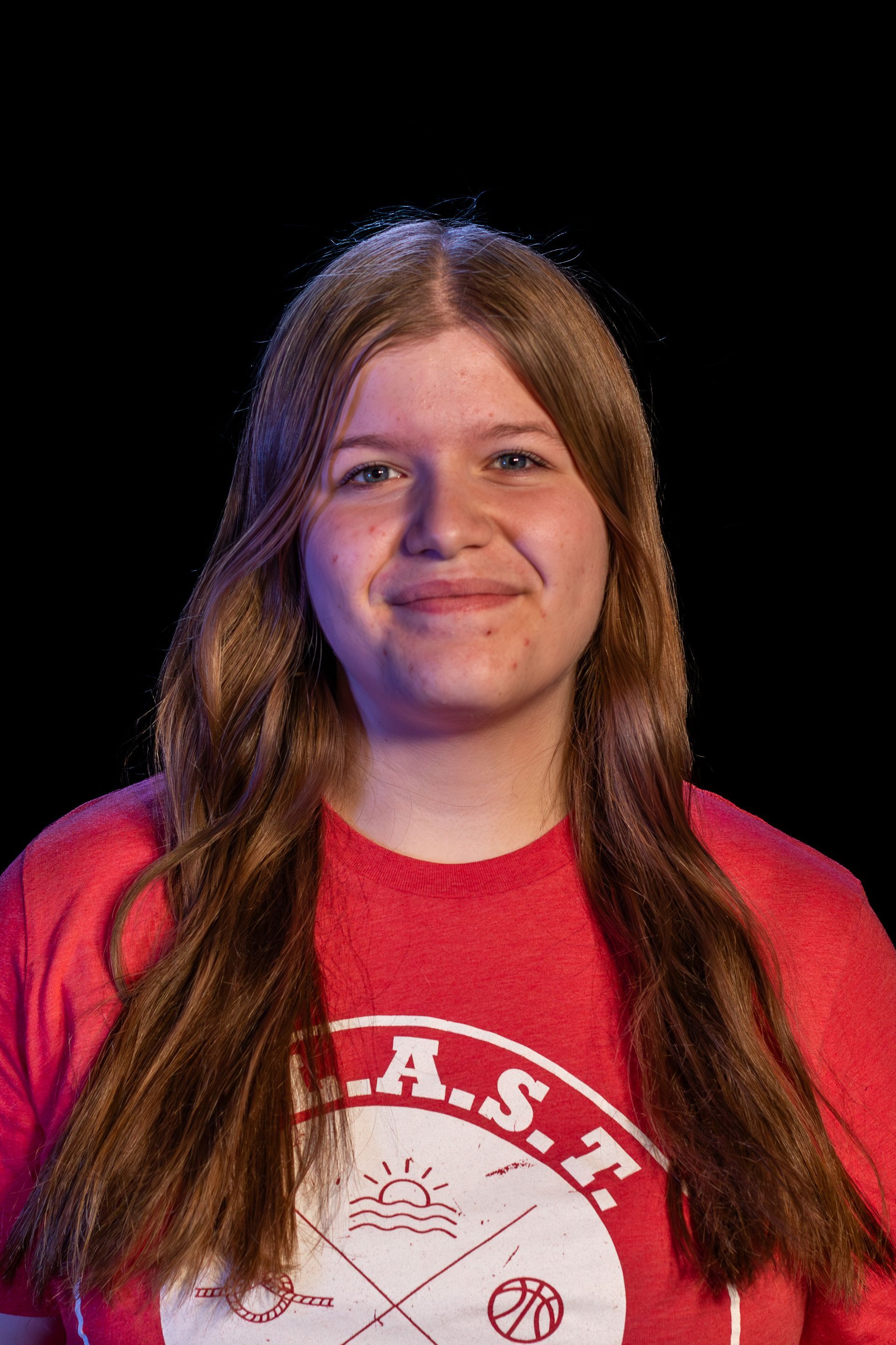 Woman in red shirt with long brown hair smiling at the camera. Black background.