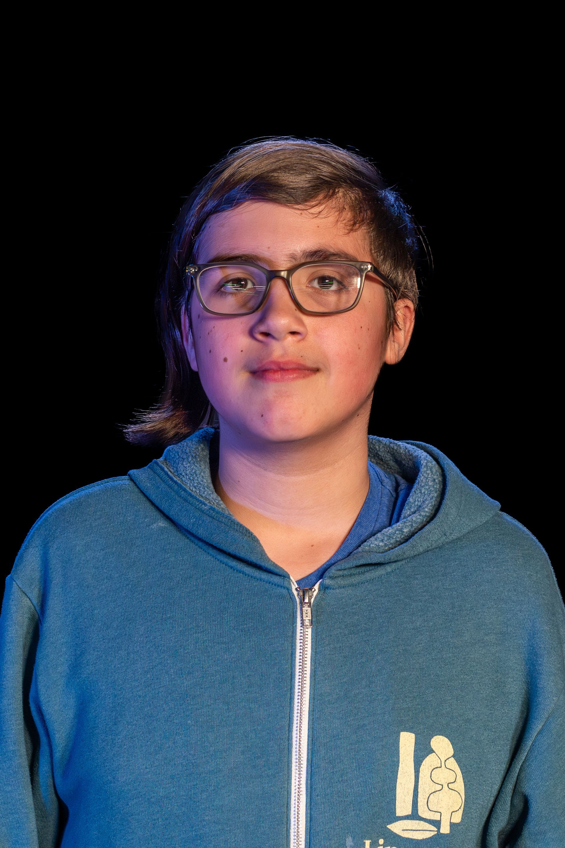 Person wearing glasses and a blue hoodie, looking at the camera. Black background.