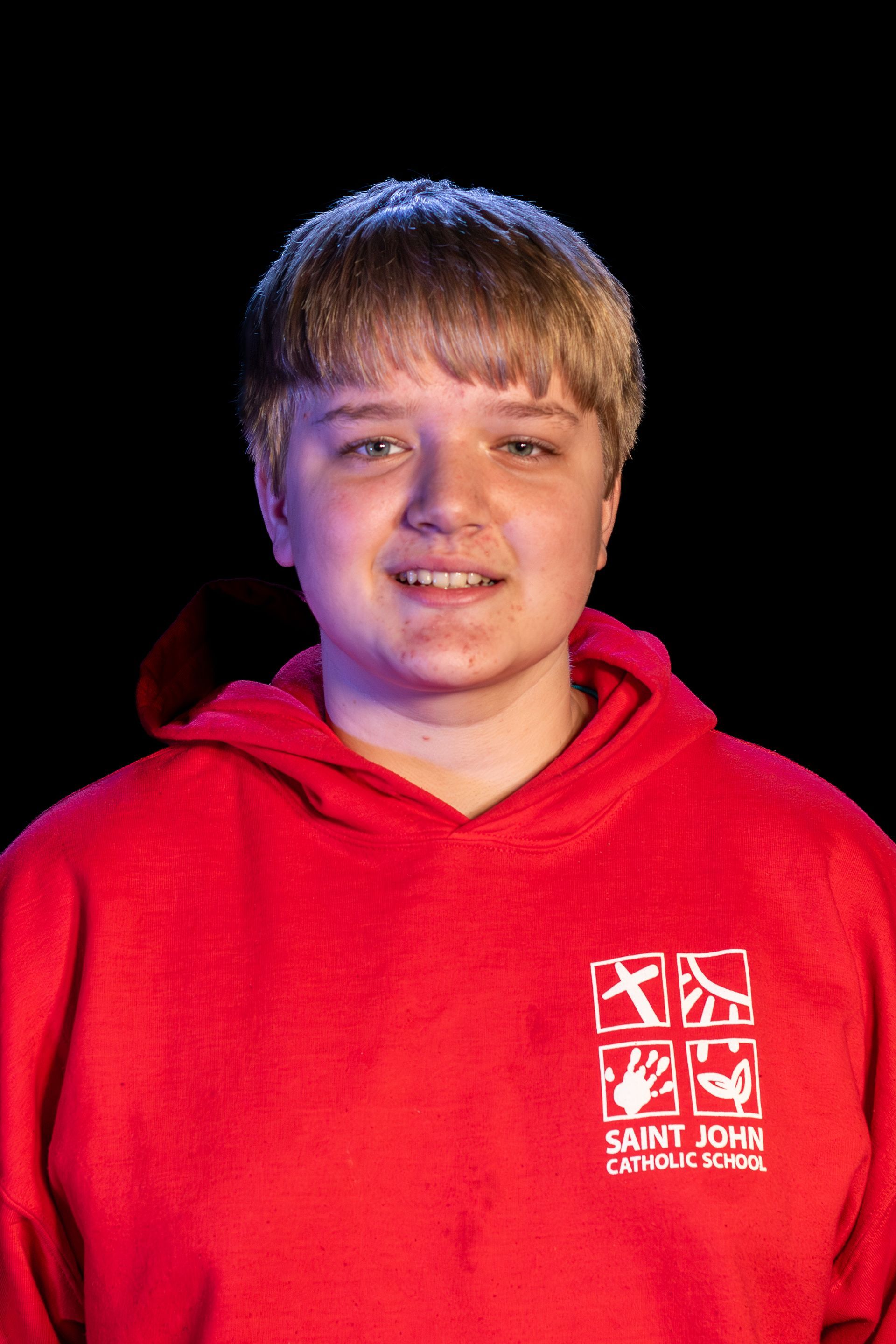 Person in red hoodie with St. John Catholic School logo, smiling against black backdrop.