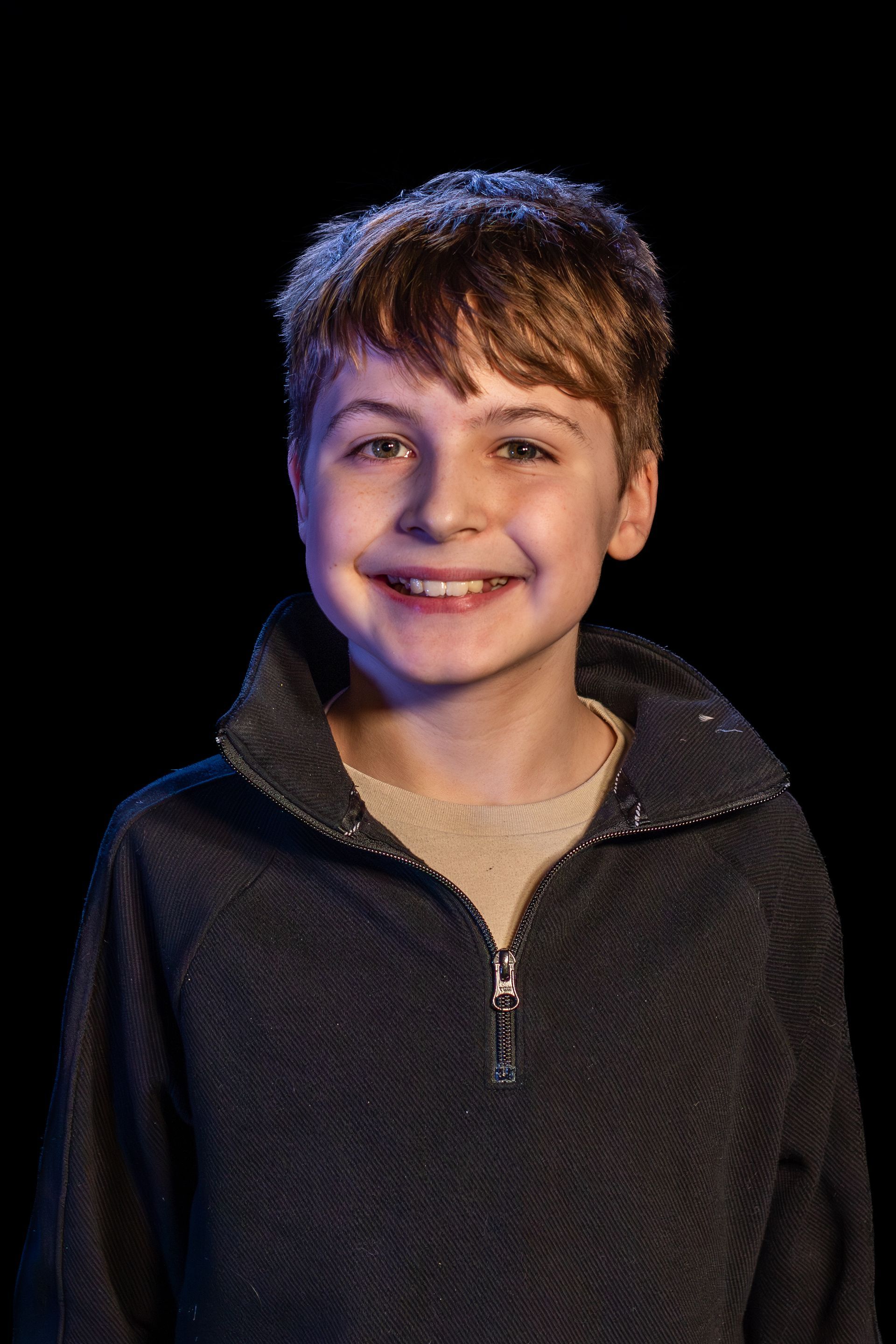Young boy with brown hair, smiling, wearing a dark blue zip-up sweater.