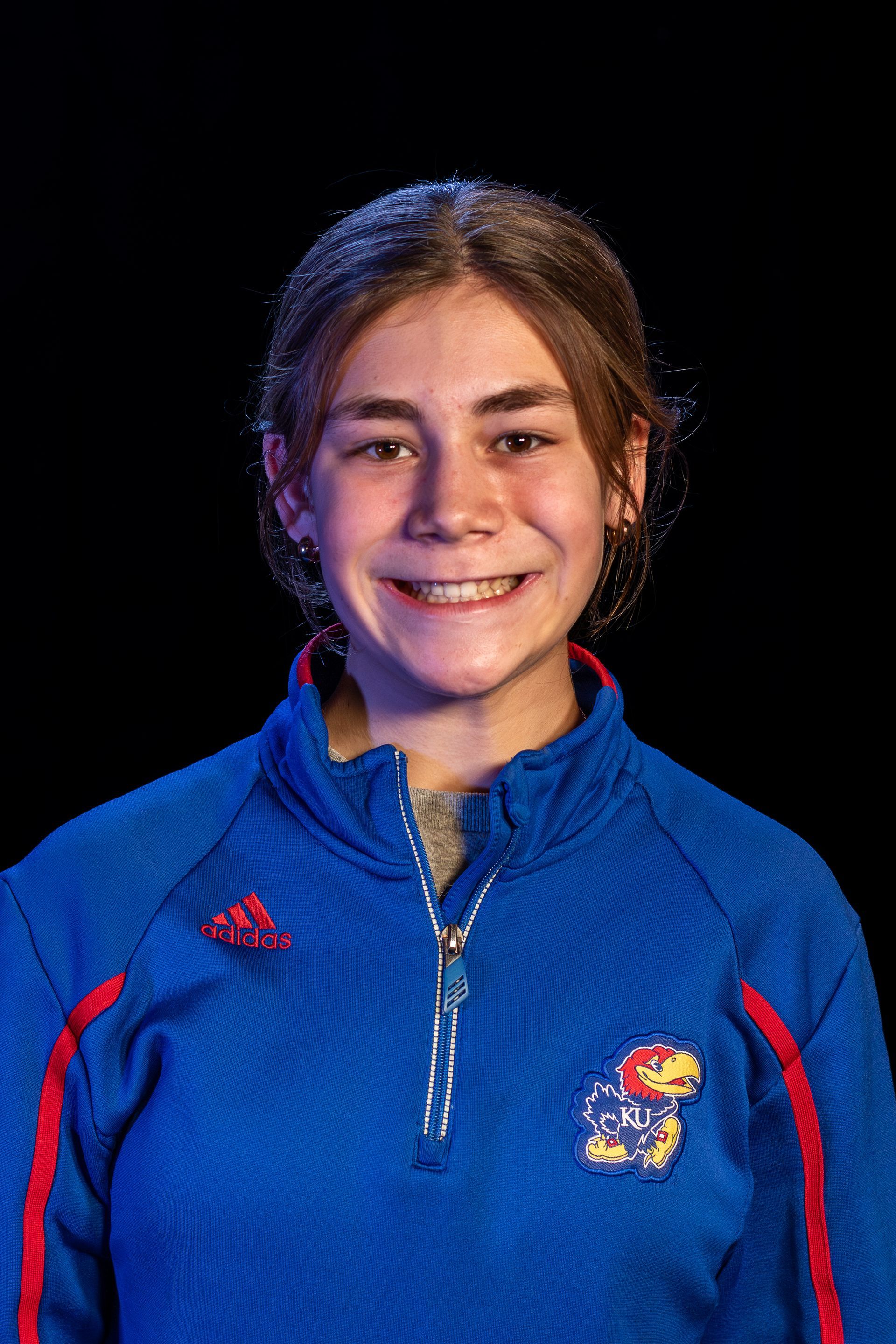 Woman in blue athletic top smiling against black background.