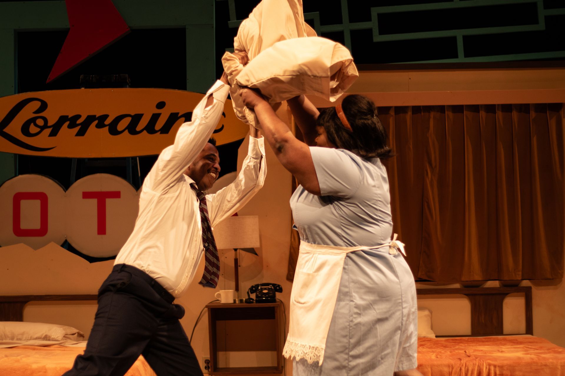 Man and woman play fight with pillows in a motel room. A