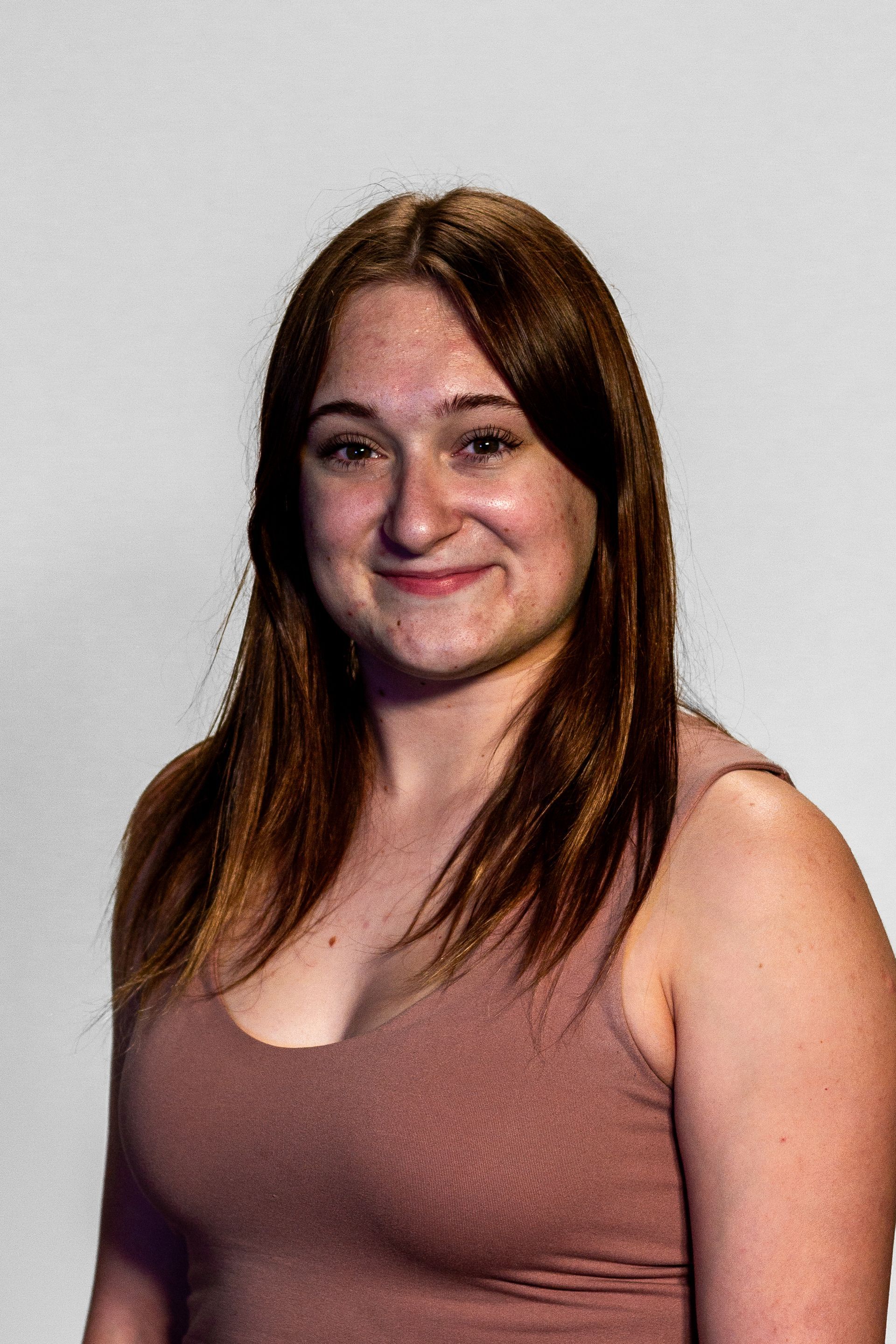 Young woman with auburn hair and a smile, wearing a mauve tank top, against a white background.