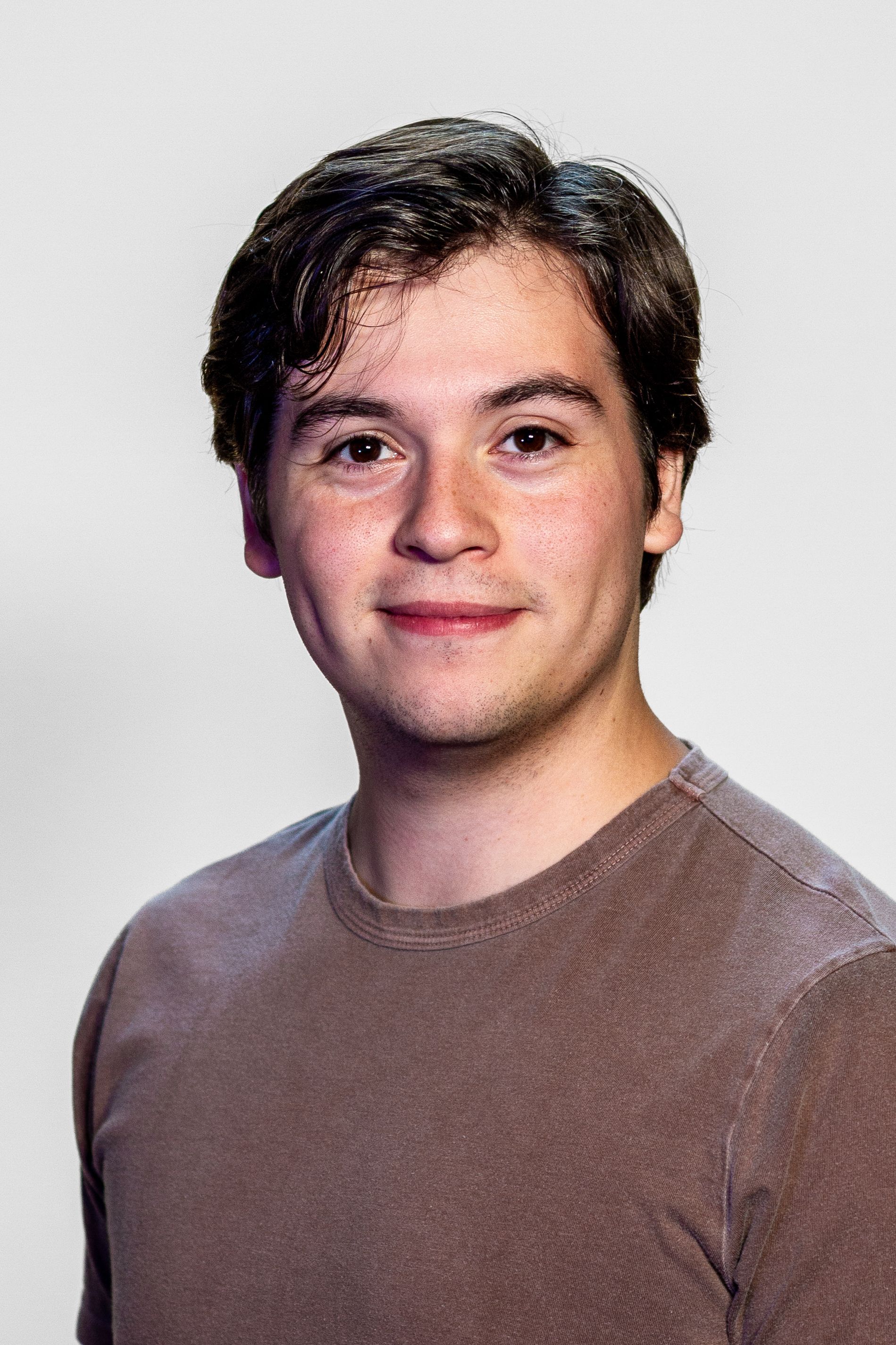 Young man with dark hair, brown shirt, smiling at the camera.