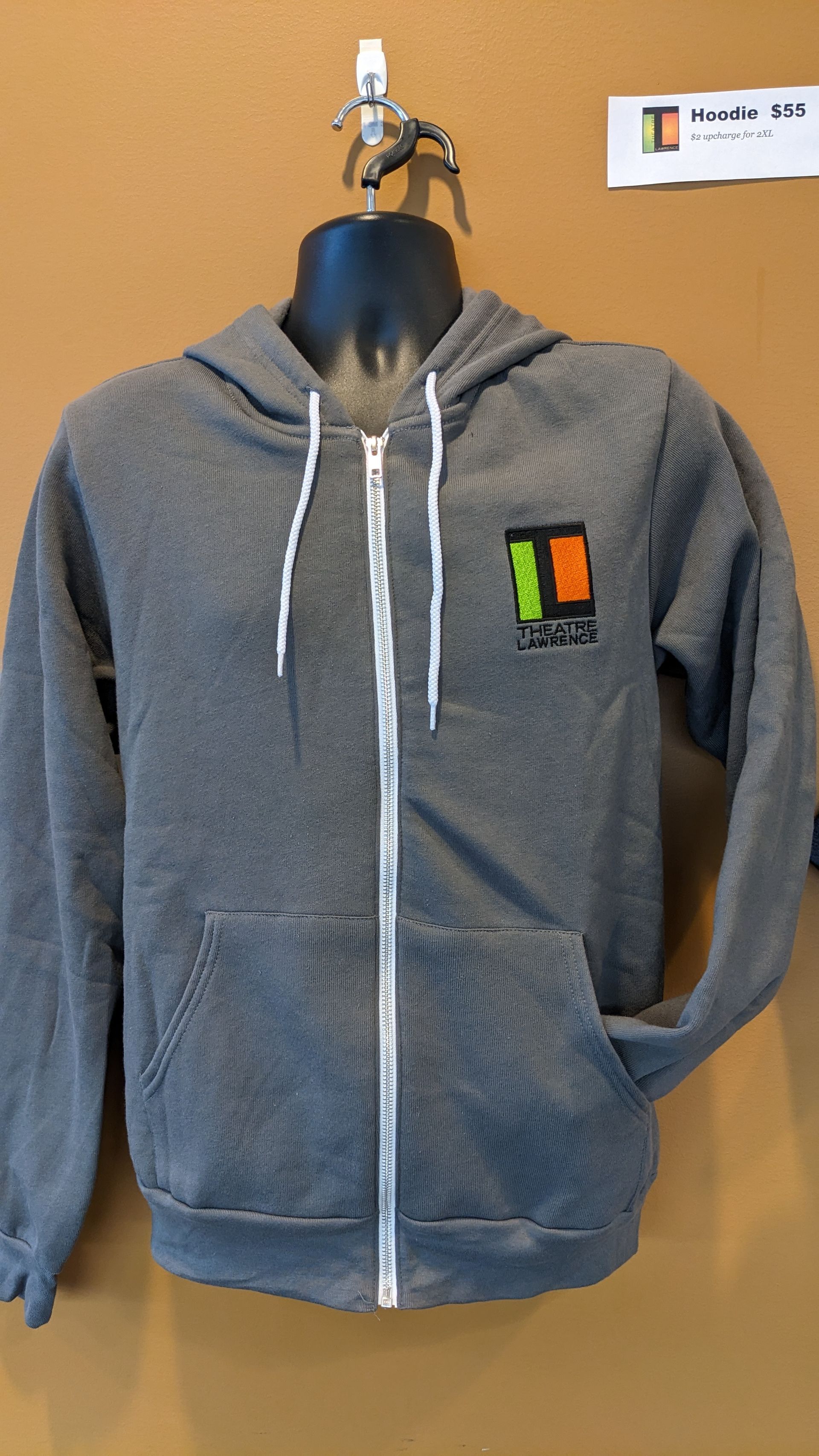 Gray zip-up hoodie with a logo on a mannequin. Background has a sign.