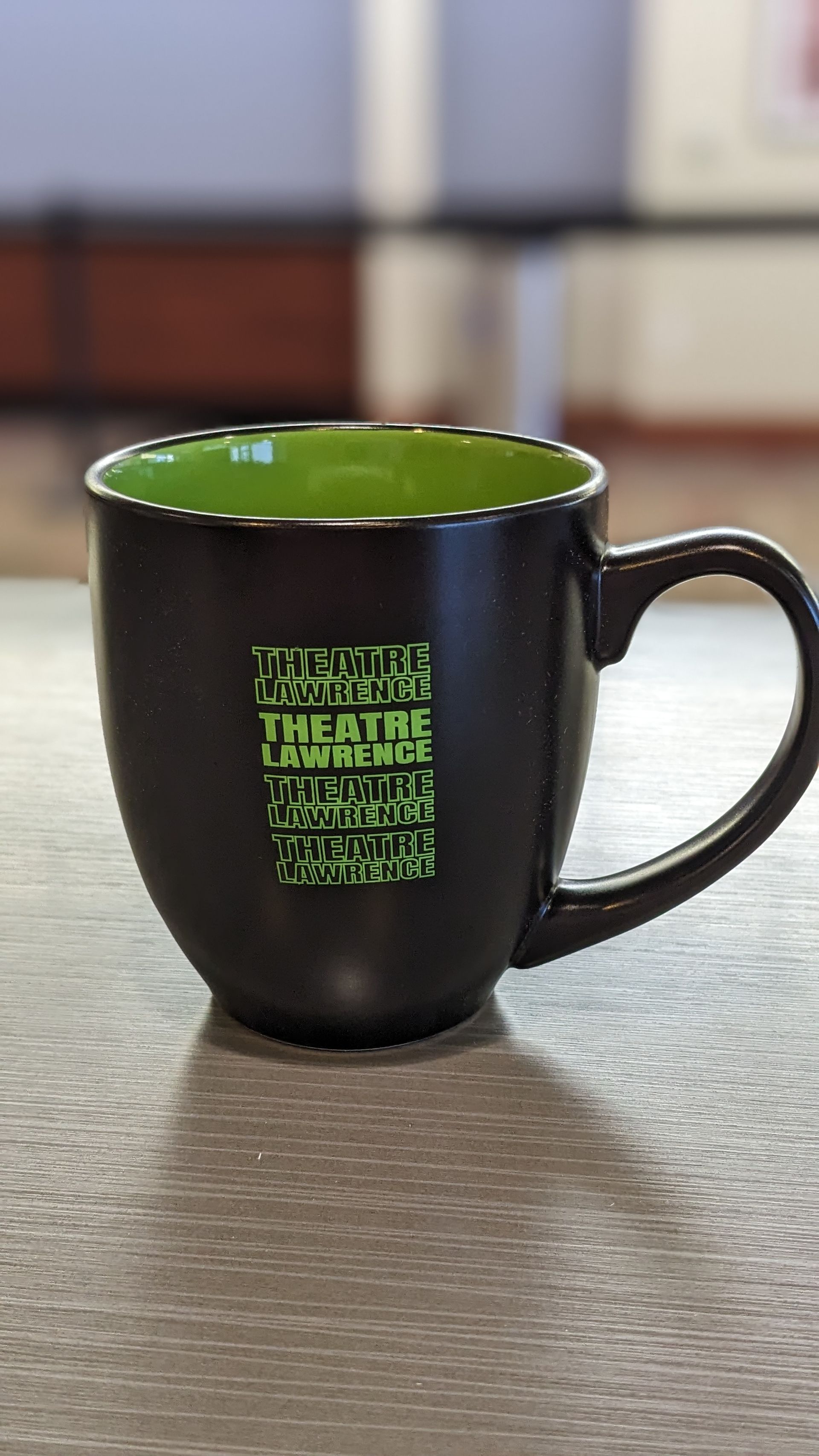 Black coffee mug with green interior and text, on a table.