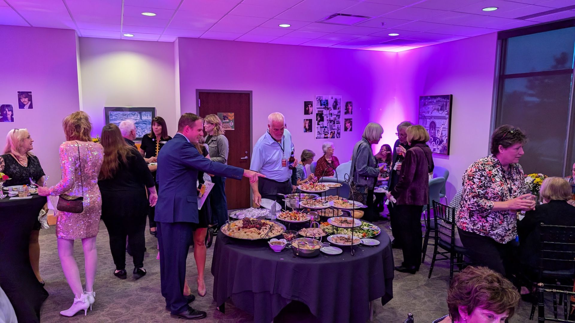 People at a party with food on a table; interior lit with purple lights.