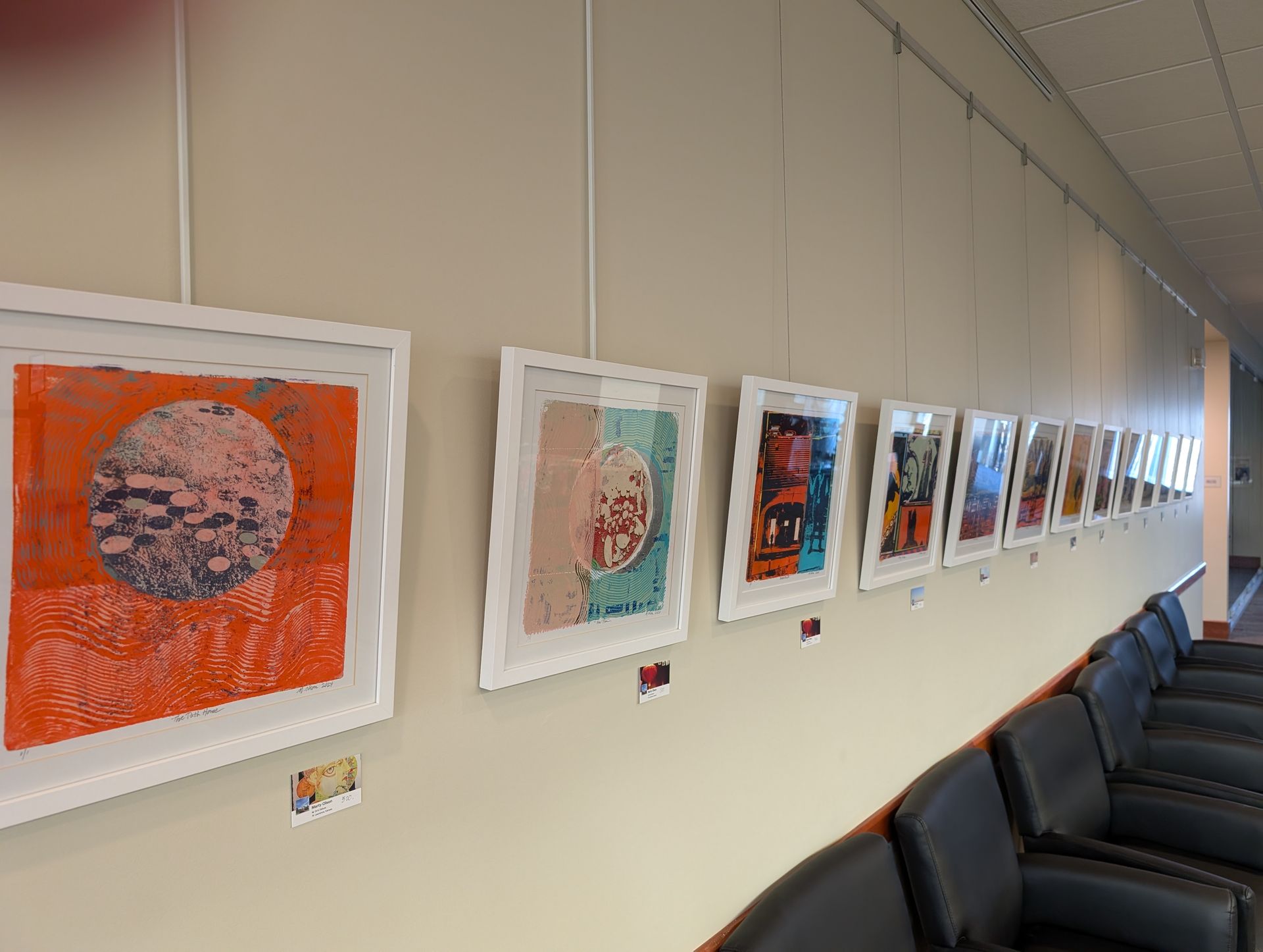 A series of framed art prints on a wall in a room, hanging above black chairs.
