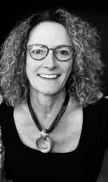 A woman wearing glasses and a necklace is smiling in a black and white photo.