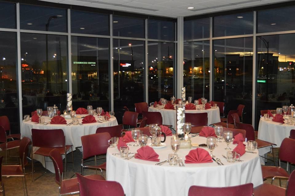 Formal dining room with round tables set with white tablecloths, red napkins, and chairs. Evening outside view.