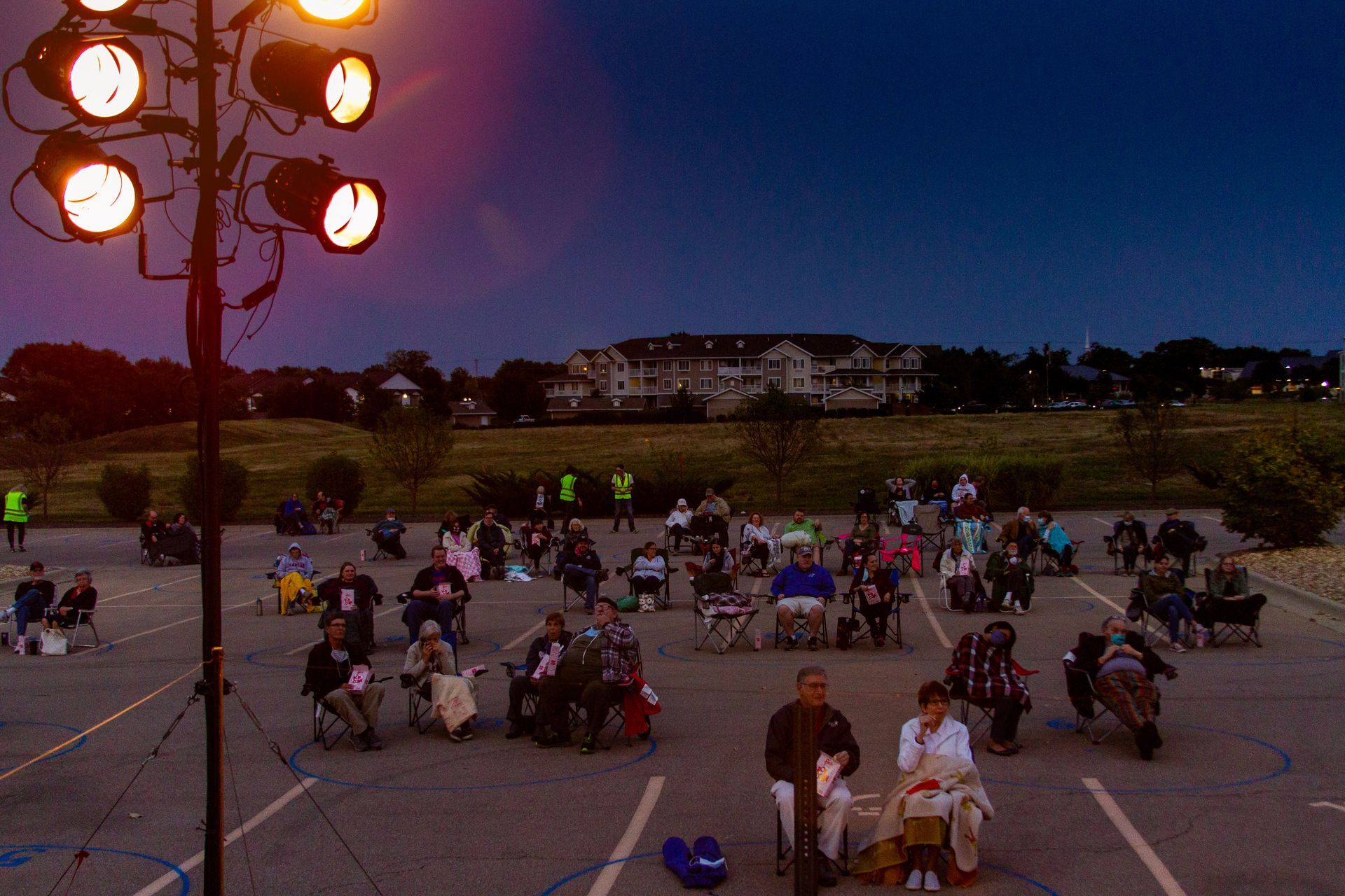 A group of people are sitting in chairs in a parking lot at night.