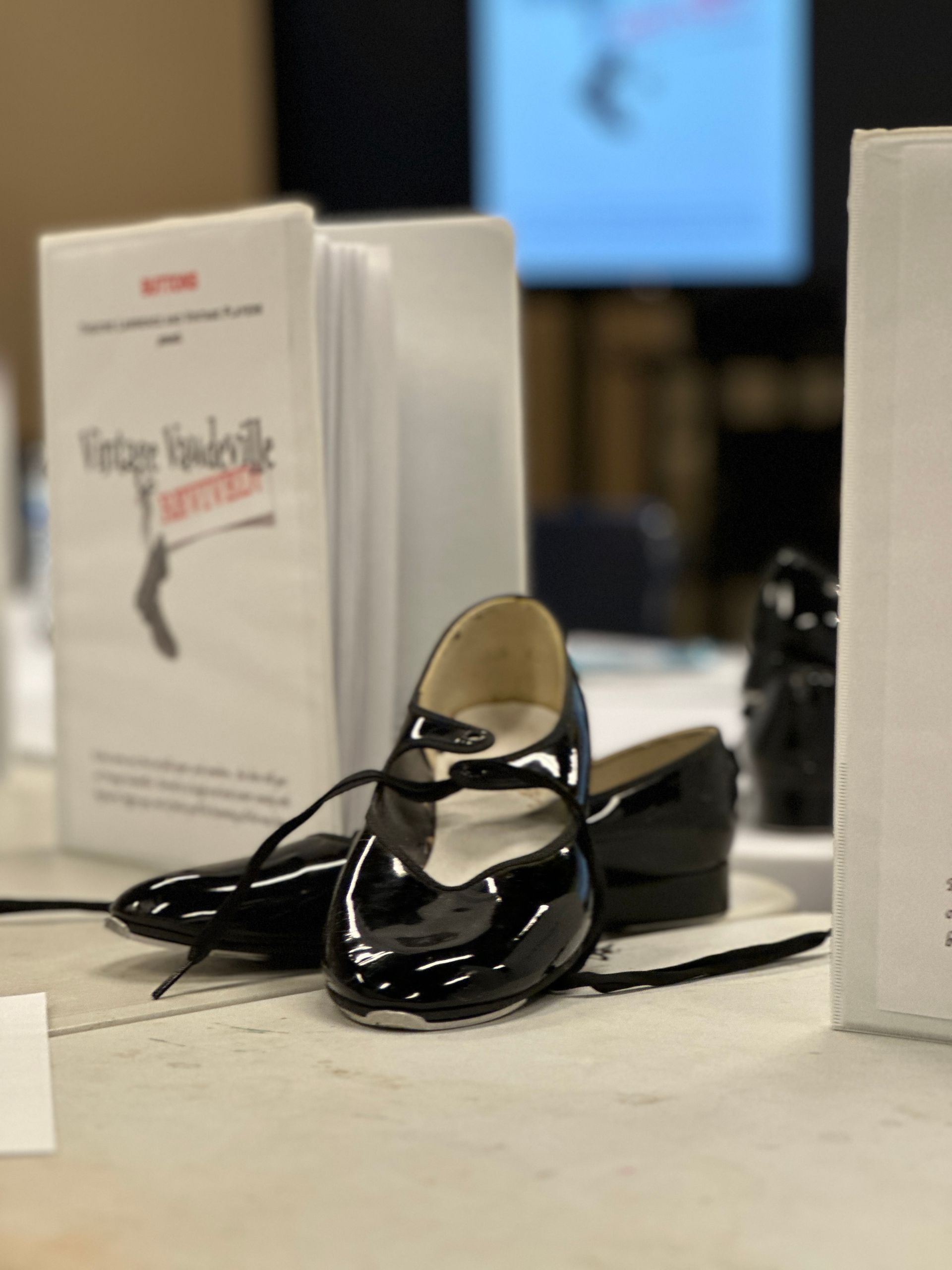 Pair of black tap shoes next to a brochure titled 