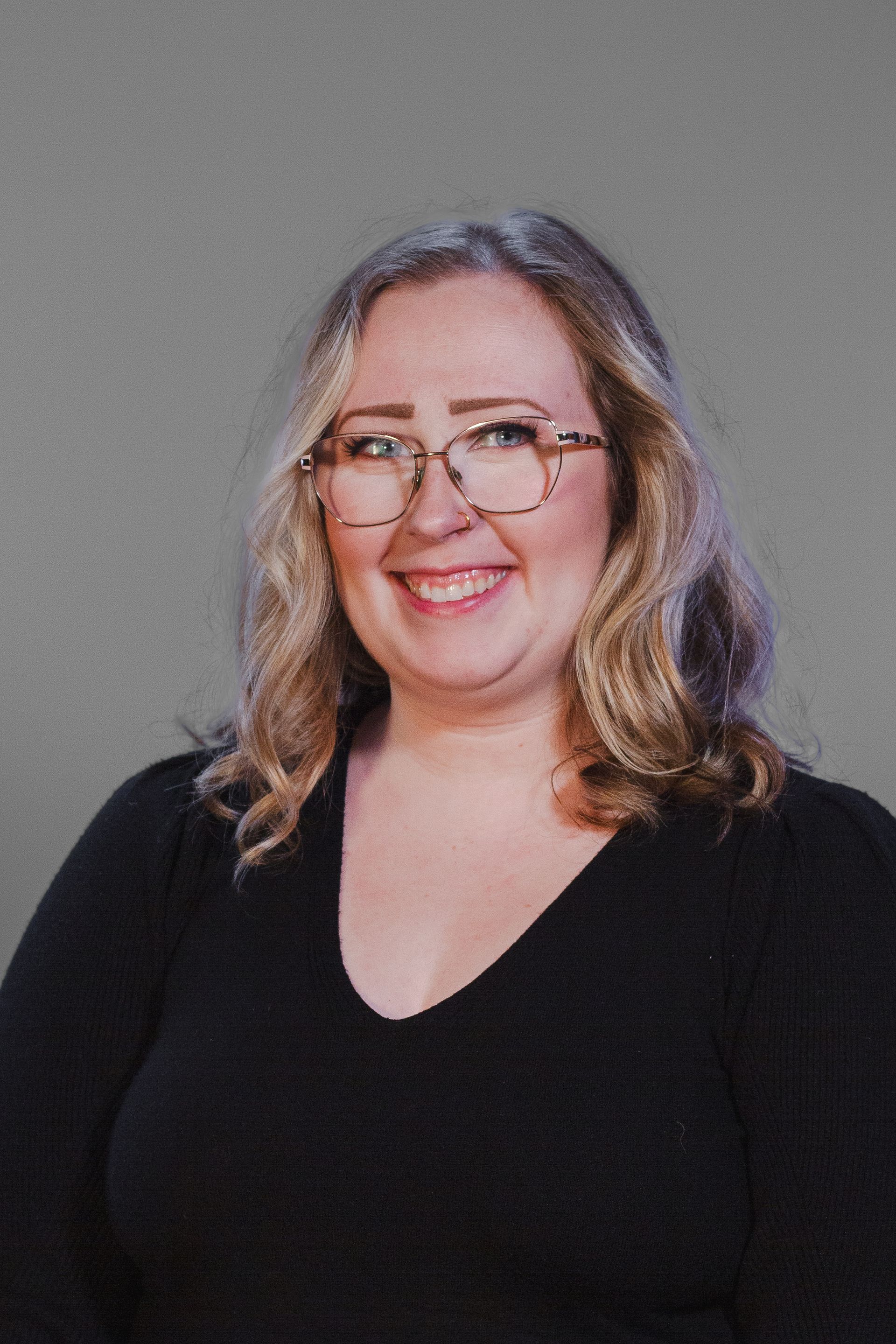 Woman with glasses smiling, wearing a black shirt, against a gray background.