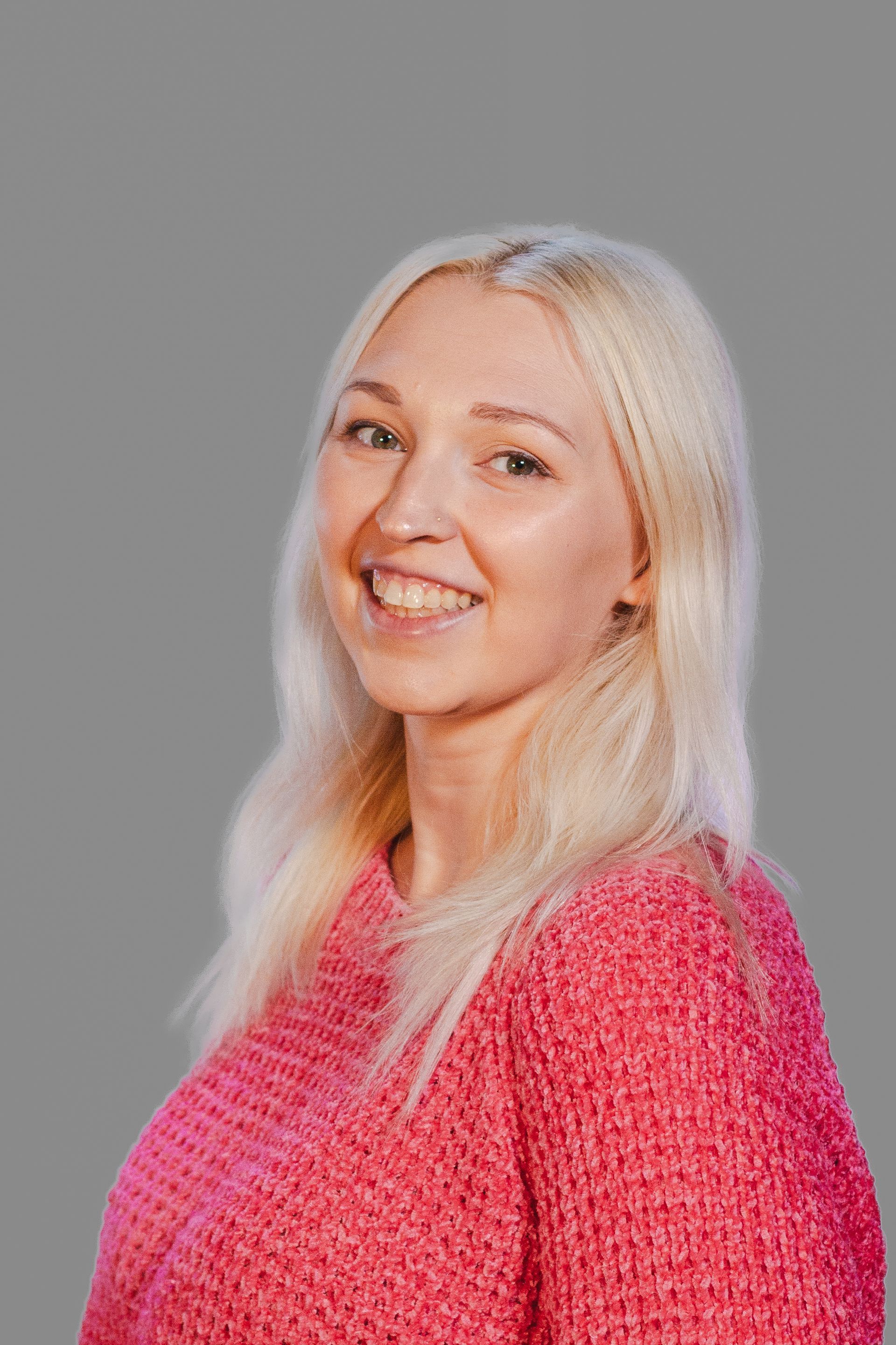 Woman with blonde hair wearing a pink sweater, smiling, facing the viewer.