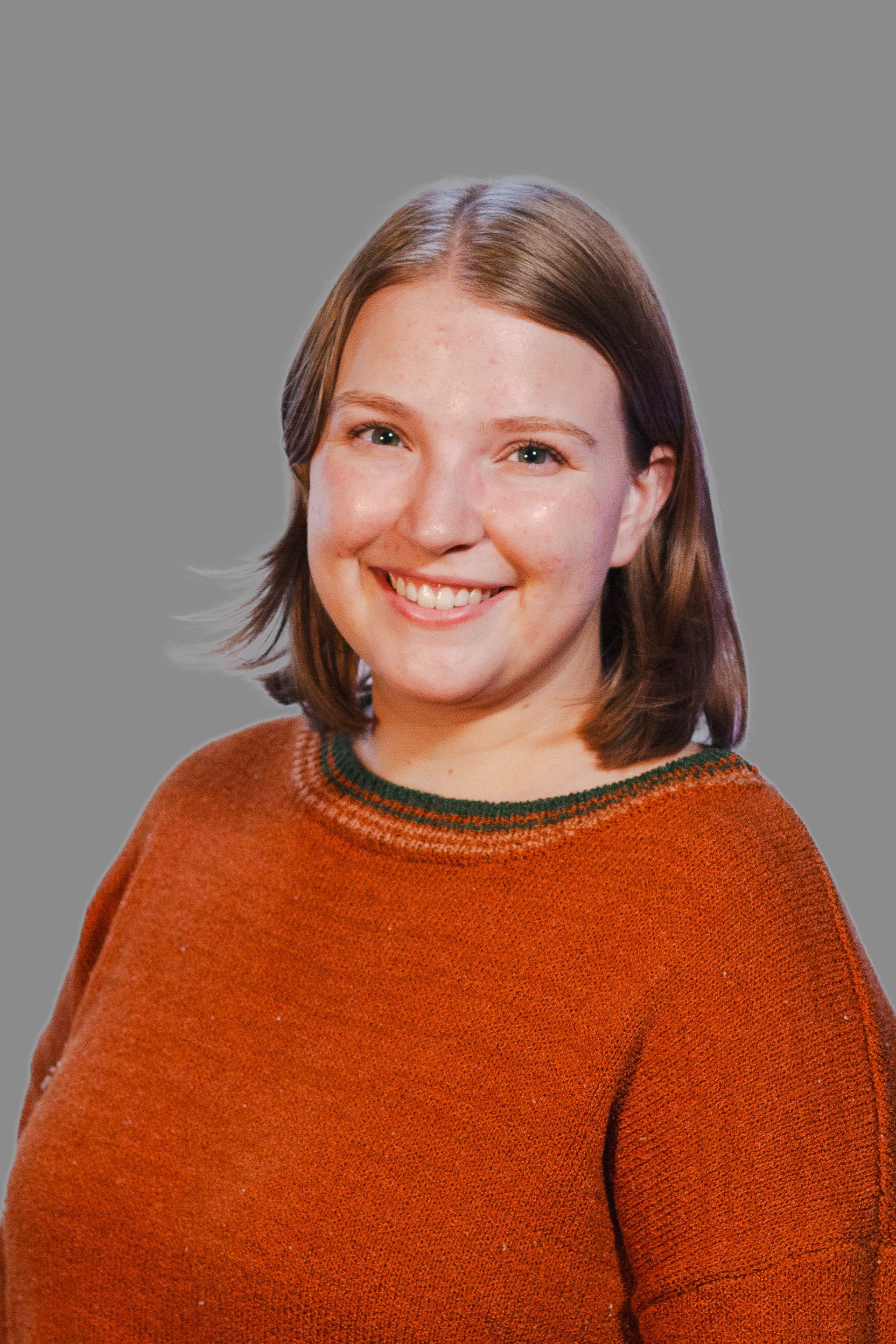 Woman with shoulder-length brown hair wearing an orange sweater smiles at the camera.