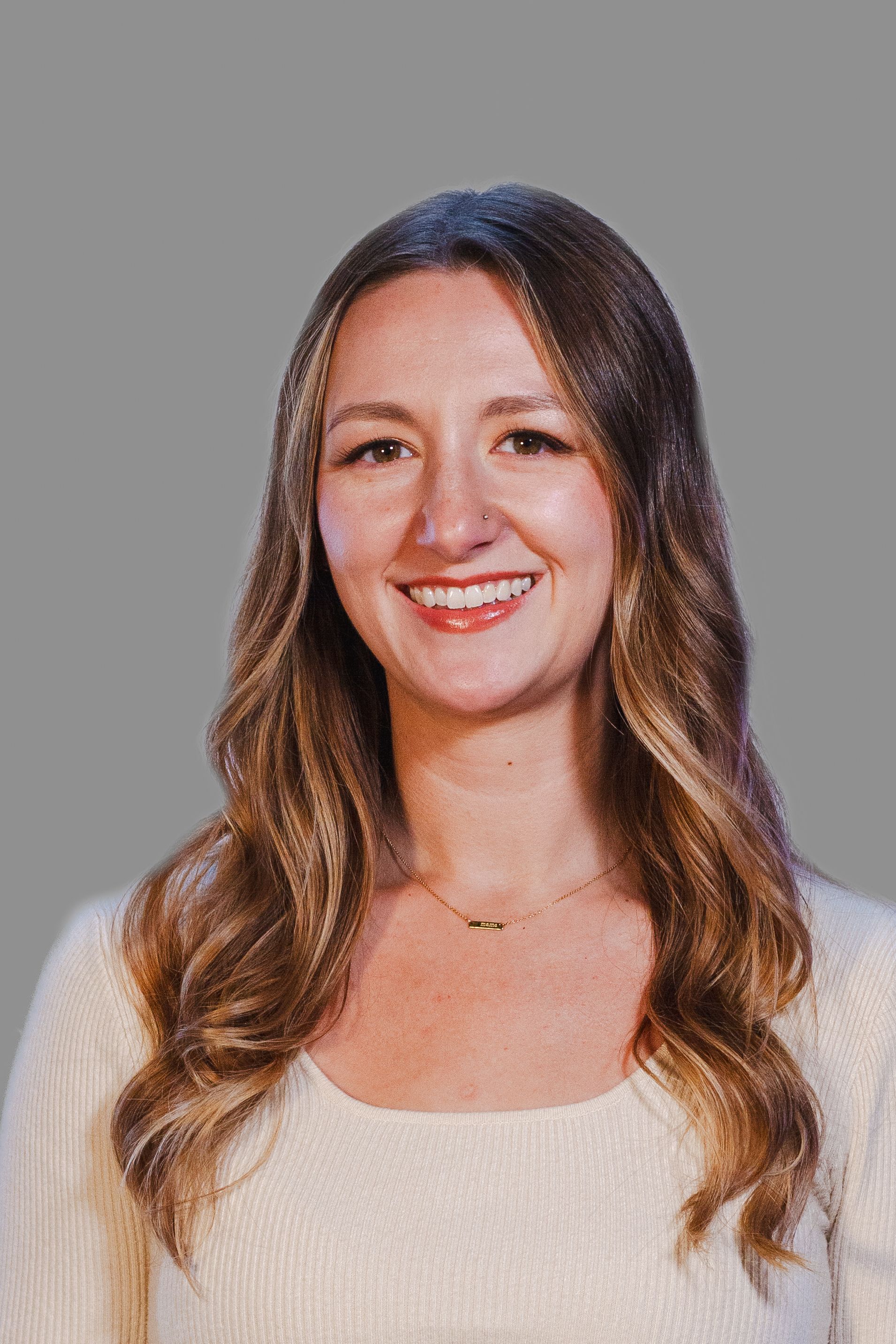 Woman with long, wavy brown hair smiles at the camera, wearing a cream sweater.