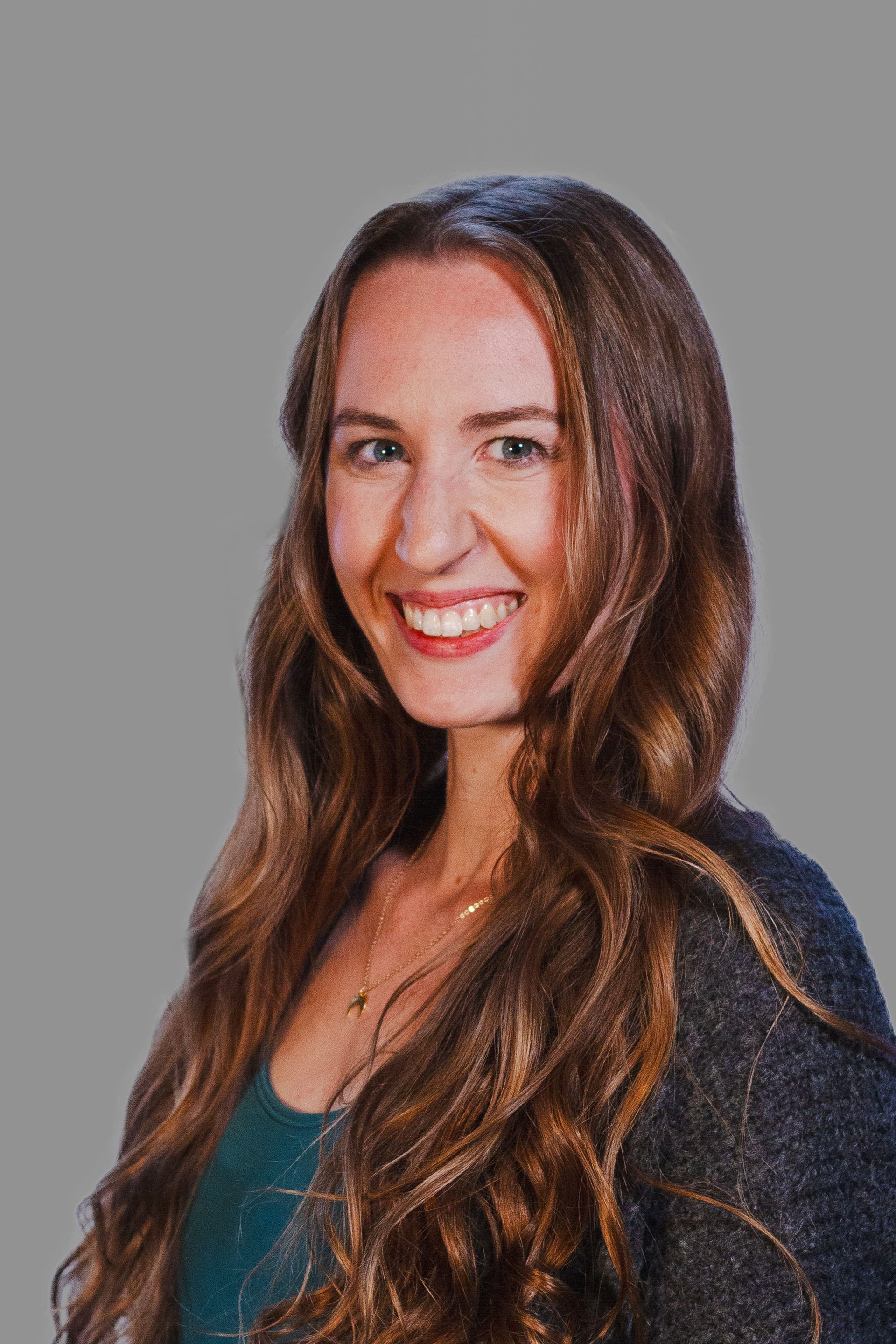 Woman with long wavy brown hair, smiling, wearing a green top and gray cardigan.