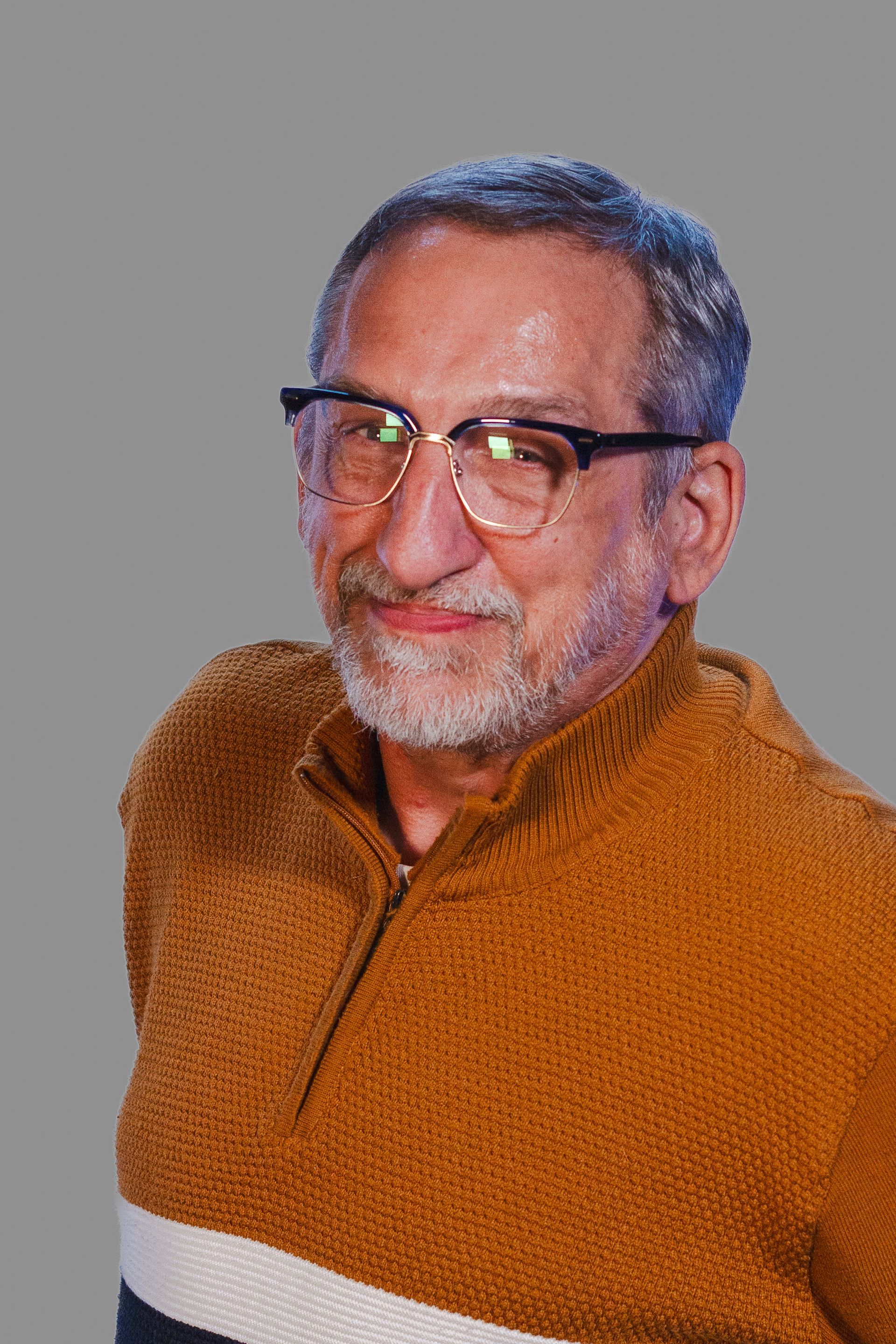 Man wearing glasses, smiling, in a brown sweater against a gray background.