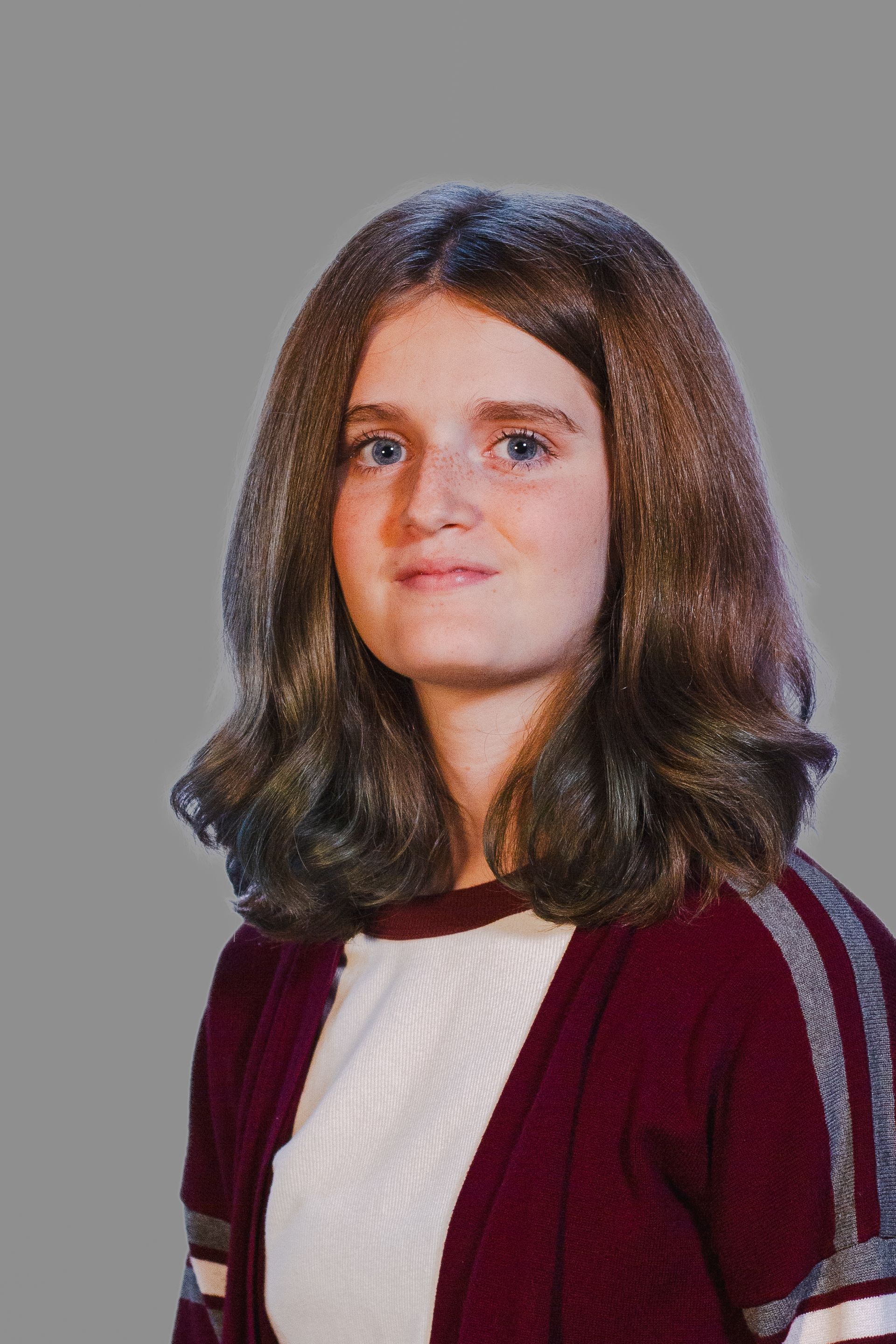 A person with wavy brown hair wearing a burgundy cardigan over a white top, looking forward.