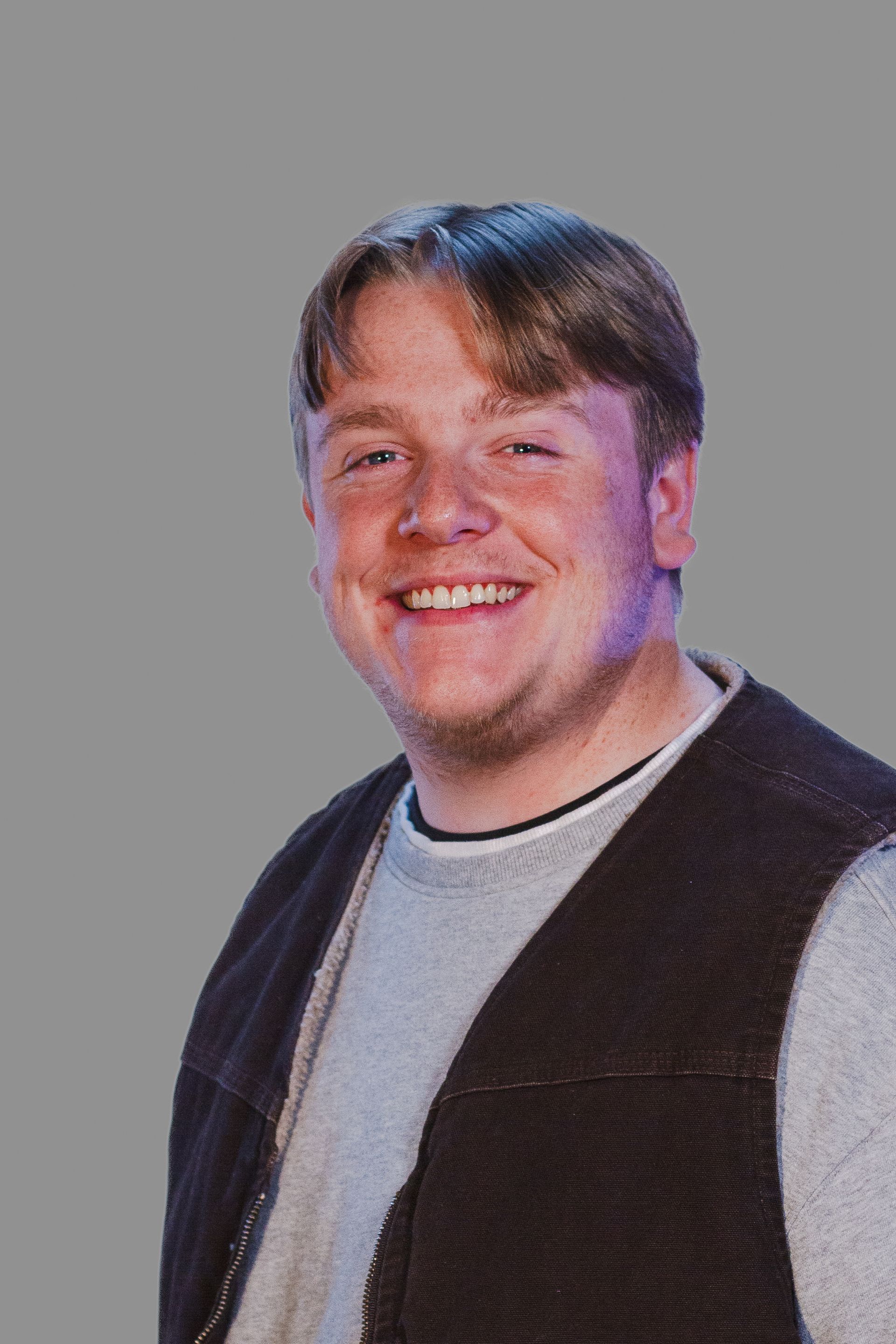 Man with fair skin wearing a gray sweater and brown vest, smiling.