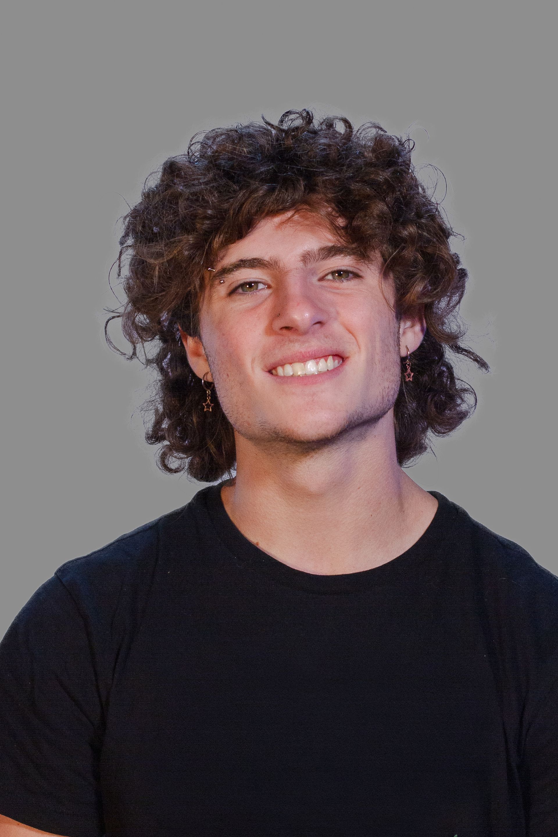 Man with curly brown hair smiling. Wearing a black shirt, set against a grey background.