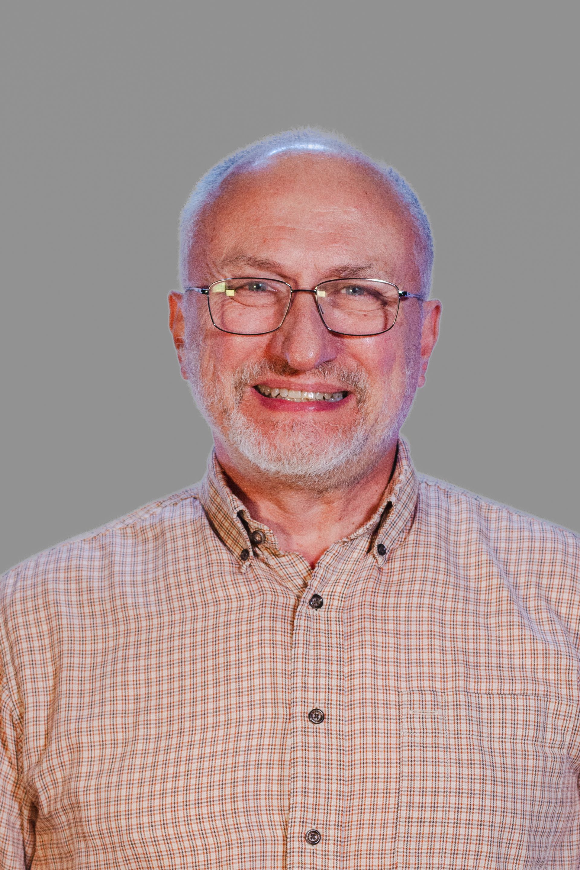 Man with glasses and a beard smiling, wearing a button-down shirt, against a gray background.