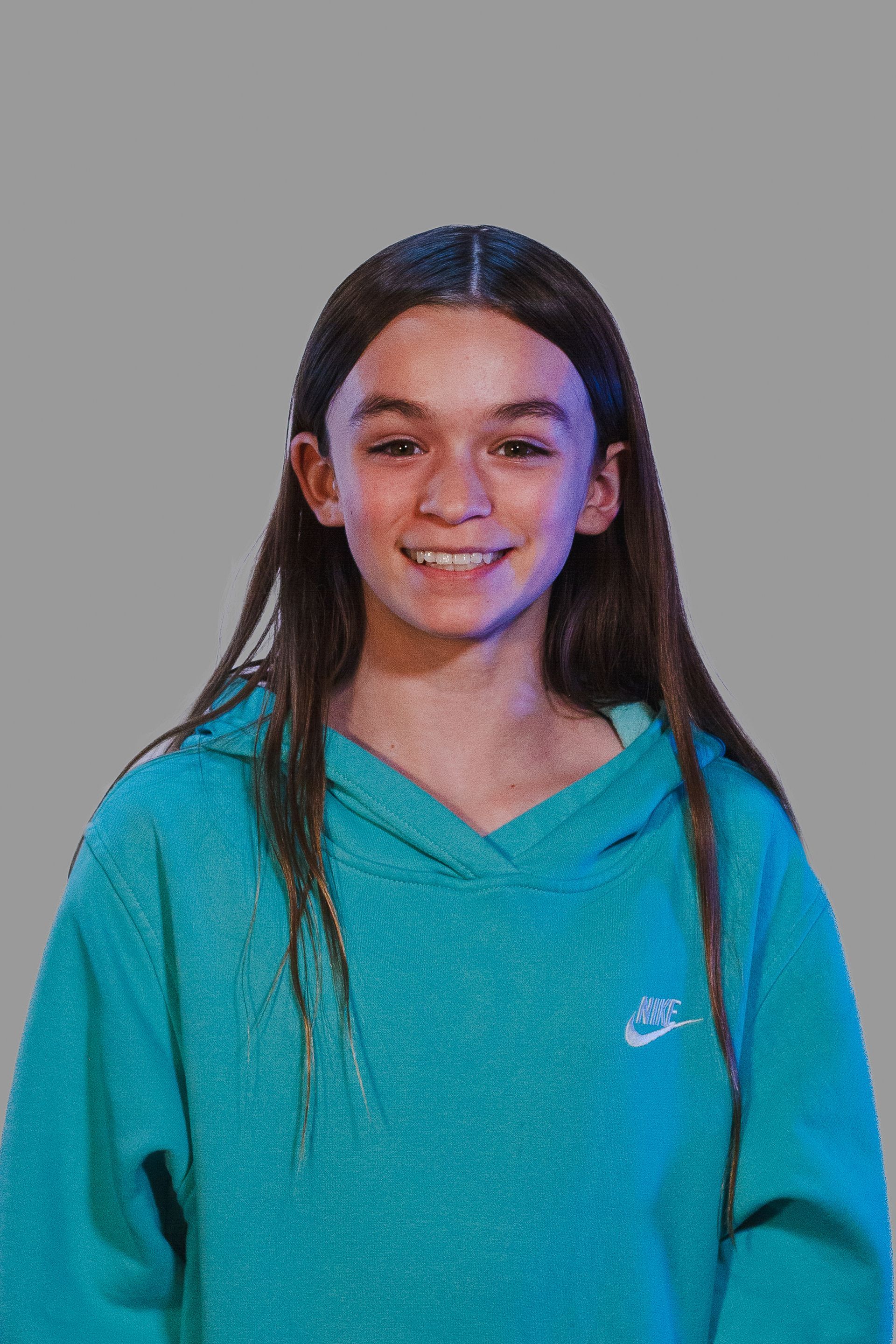 Girl smiles wearing a teal Nike hoodie; gray background.