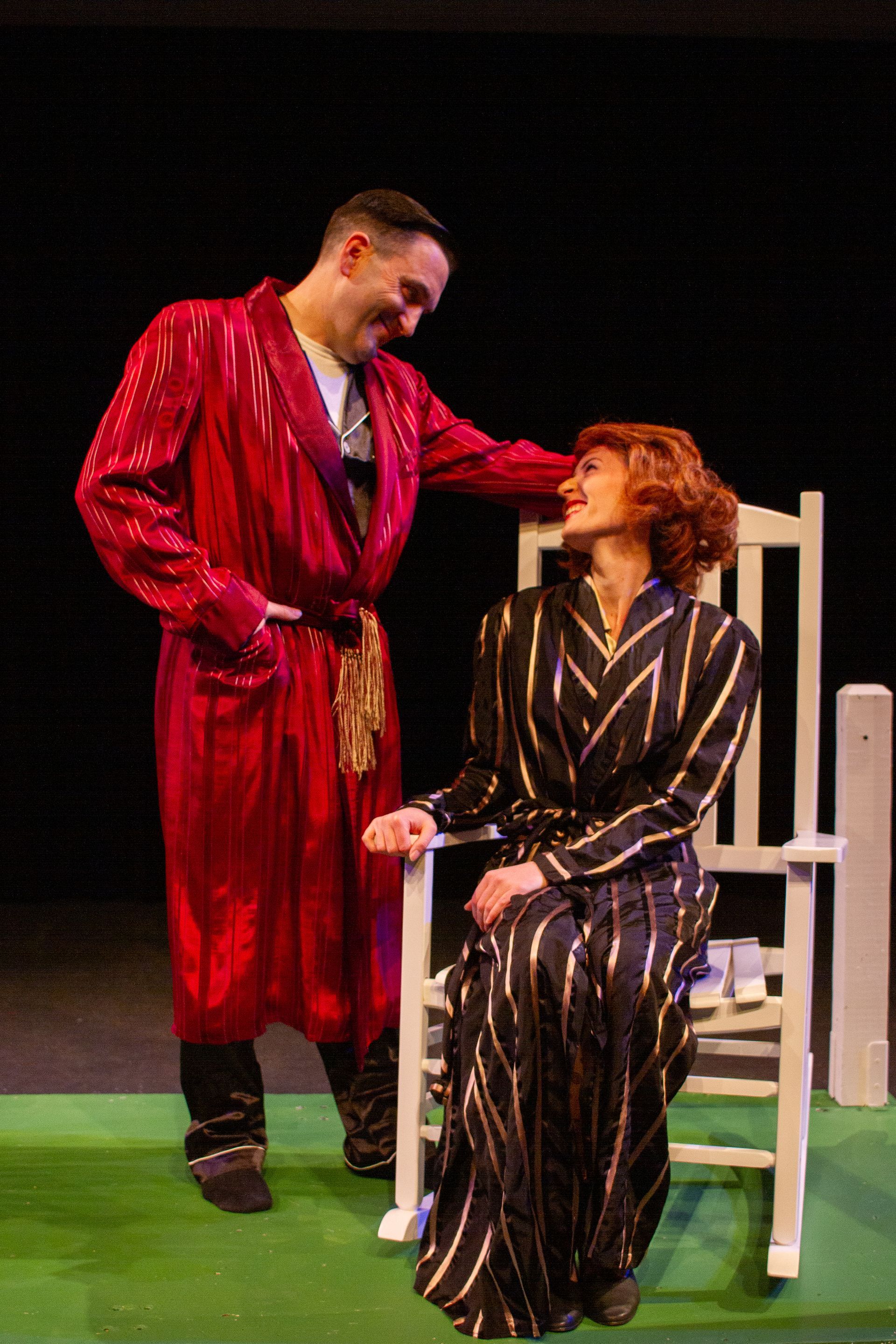 Man in red robe smiles at woman in rocking chair wearing black and gold robe.