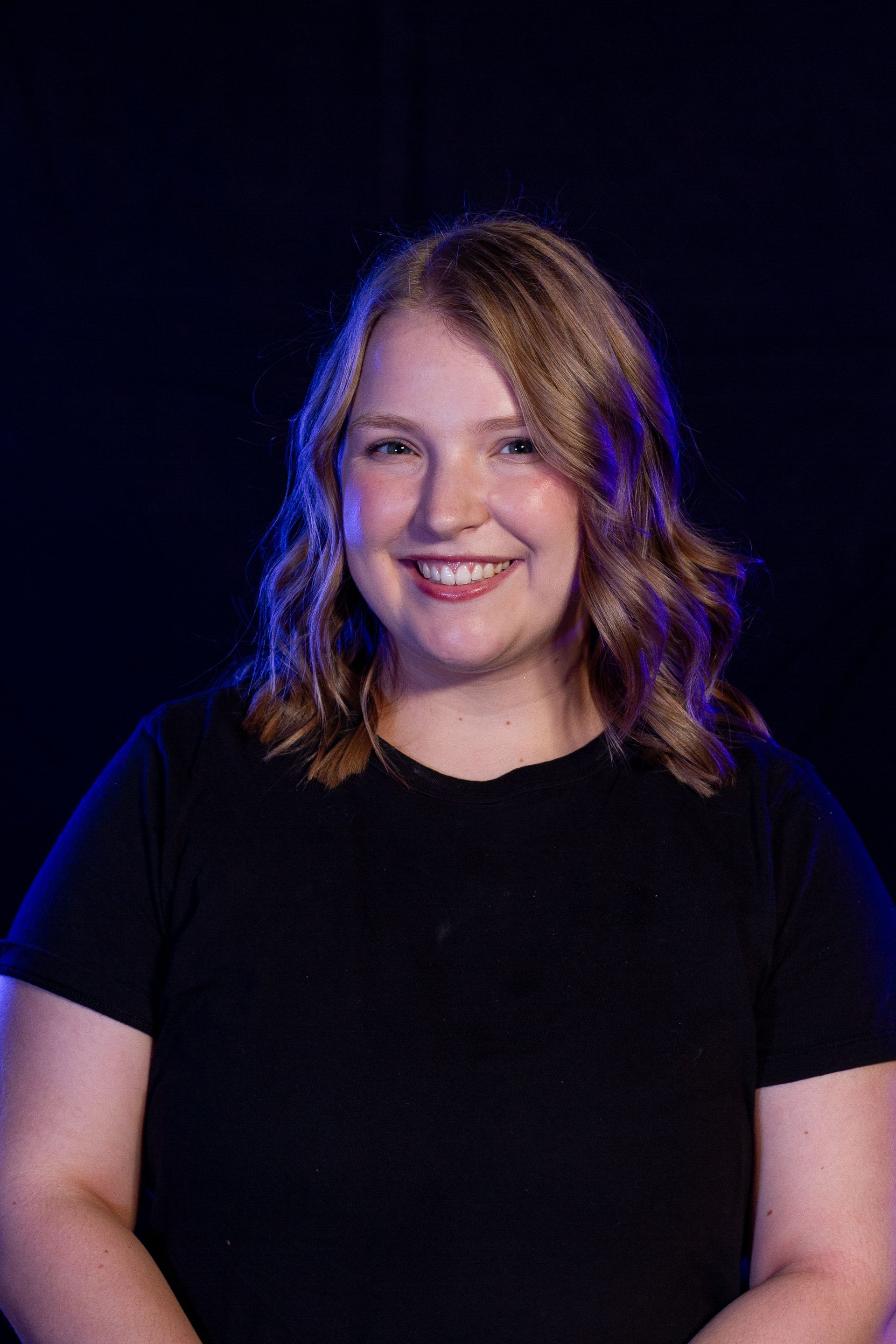 Woman with blonde hair smiles against a dark blue background, wearing a black shirt.