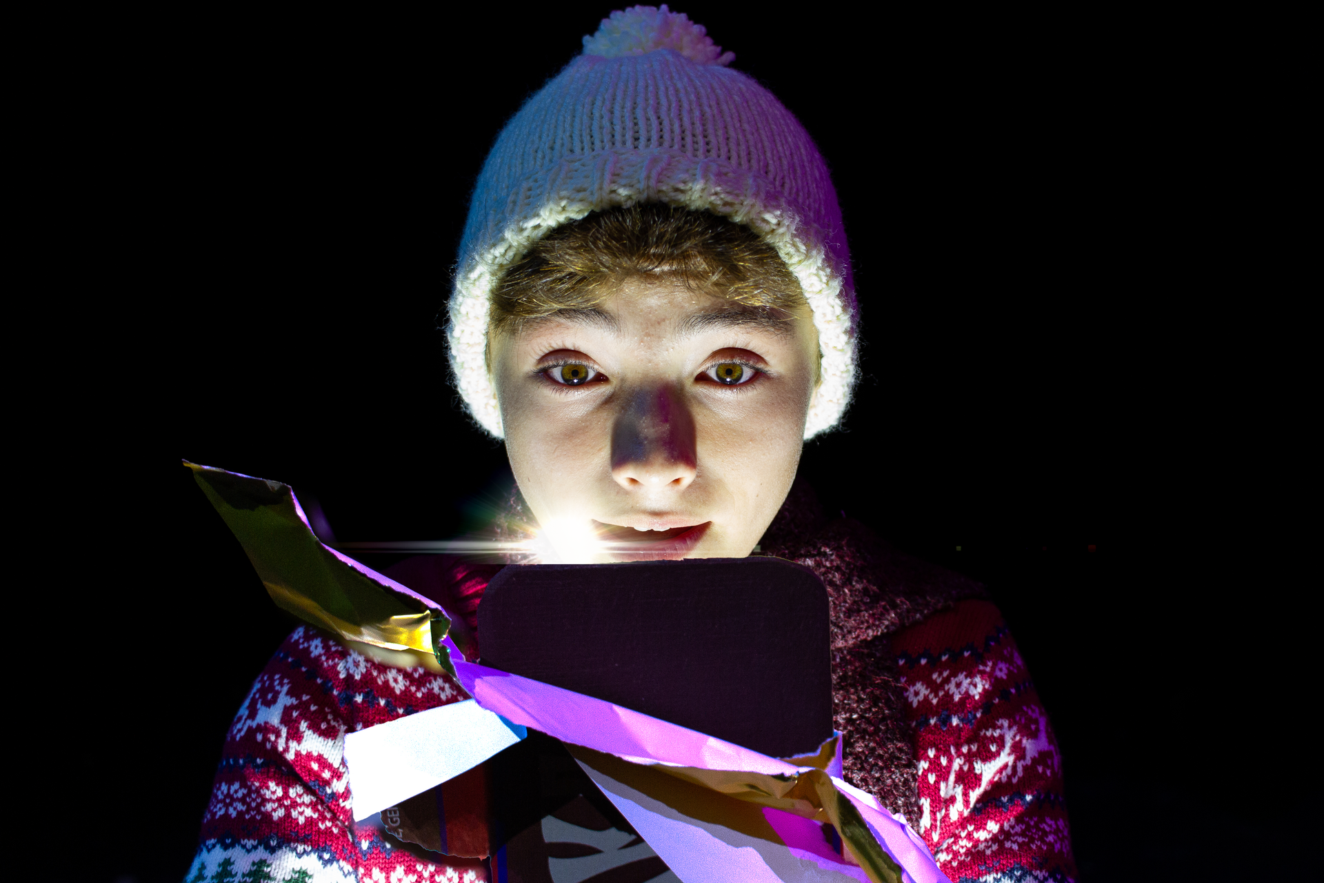 Young person in hat illuminated by colorful light emanating from a device.