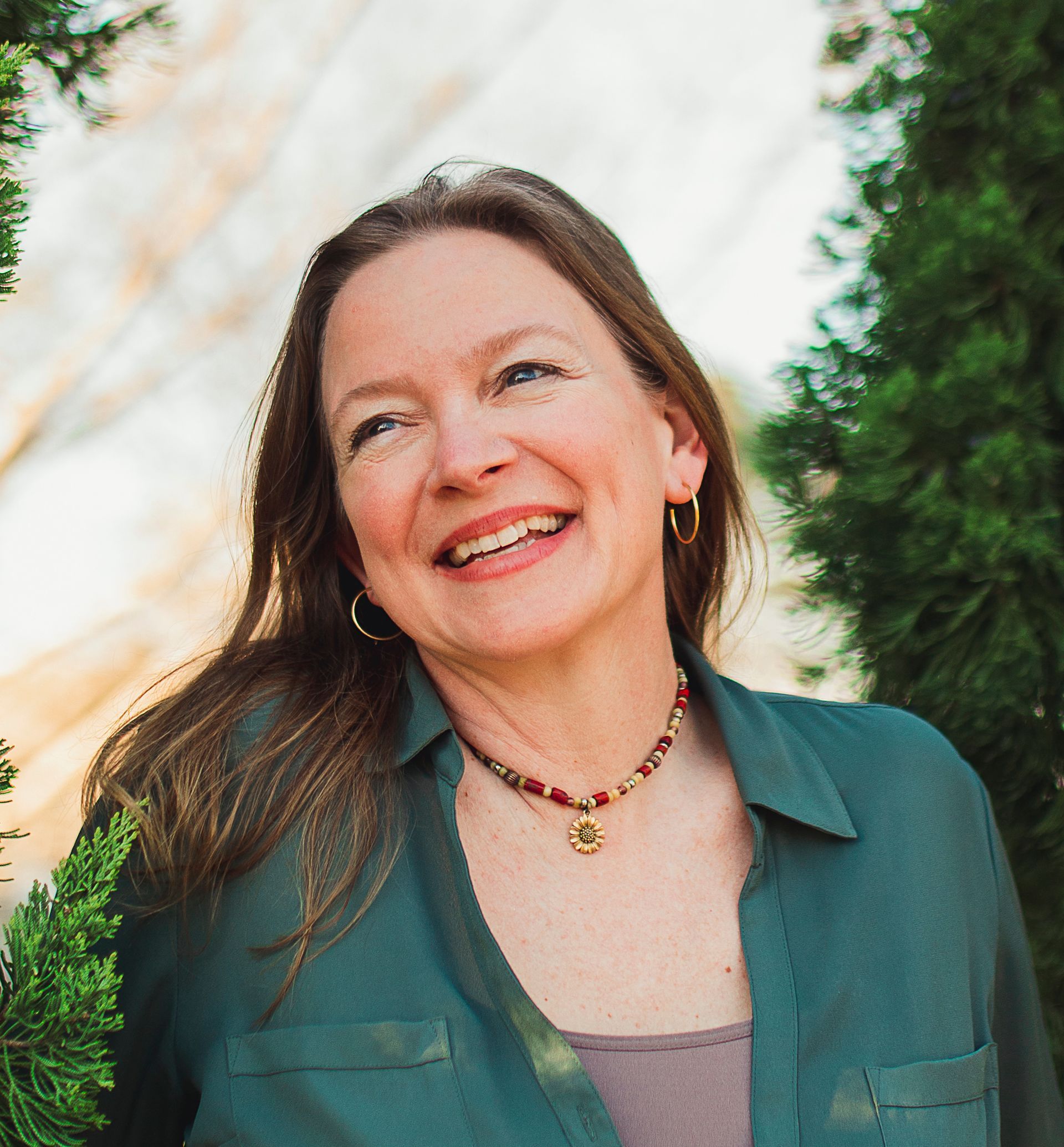 Smiling woman with long hair, wearing a green shirt and necklace, outdoors.