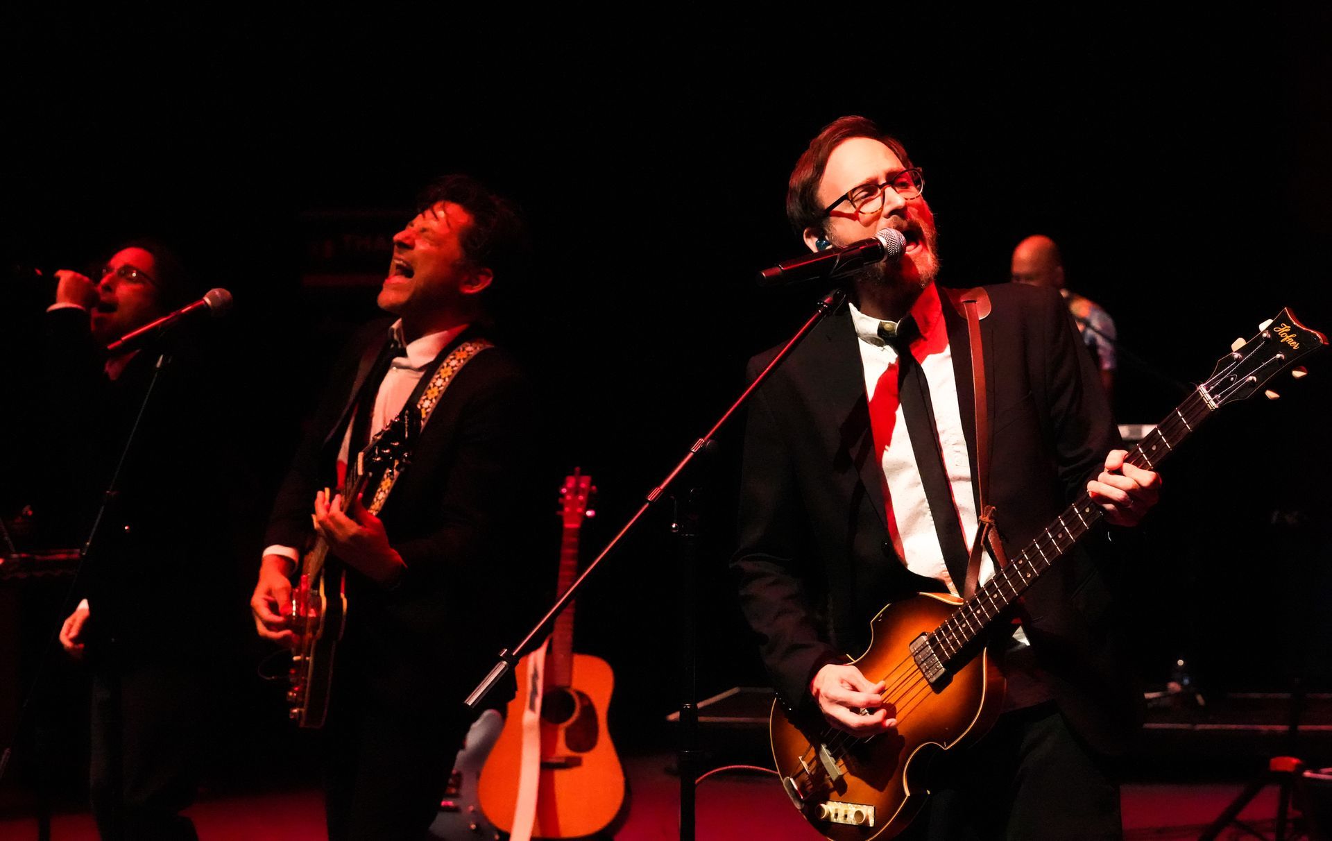 Band performing on stage, guitarist singing, other musicians in background.