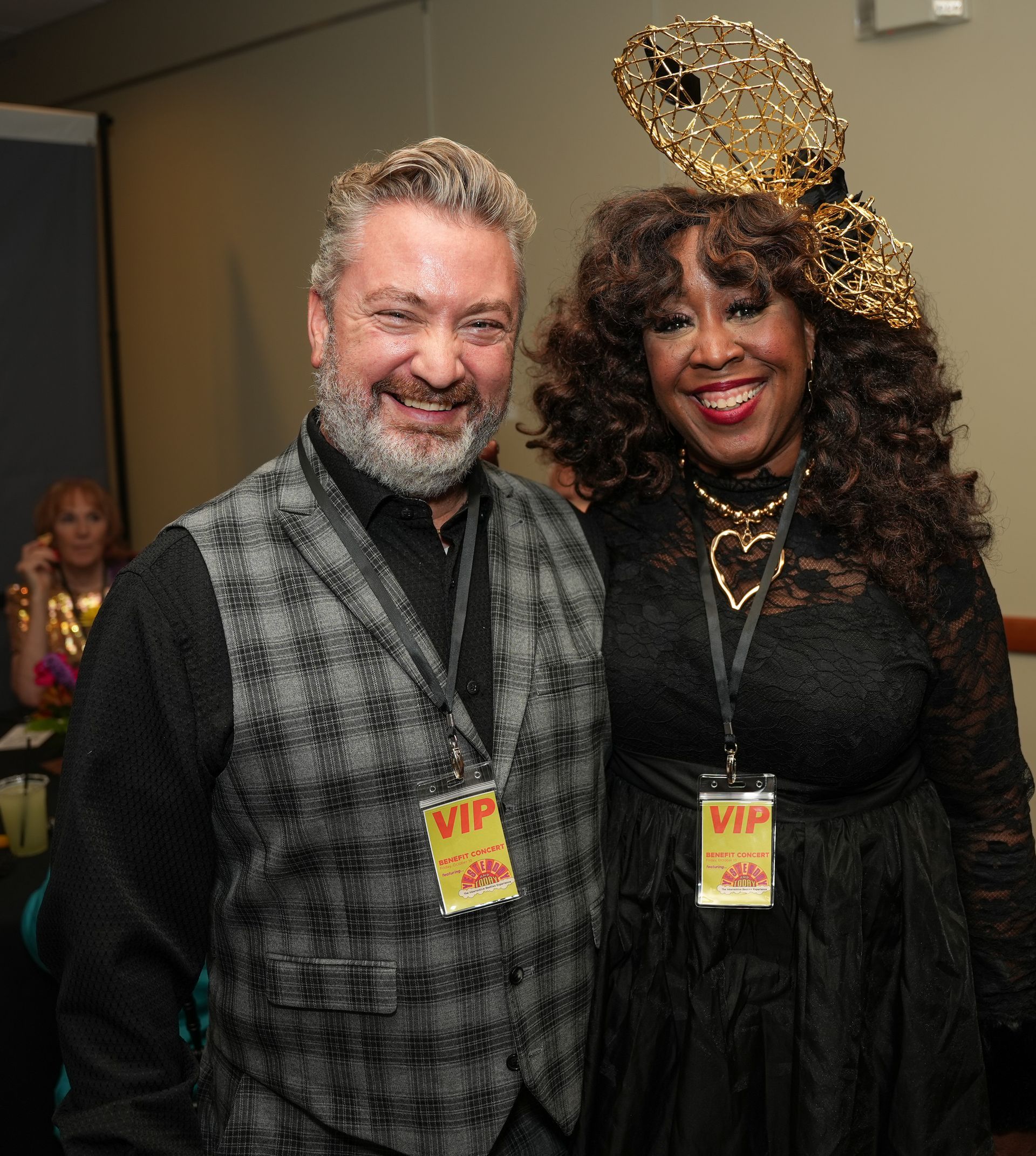 A man and a woman stand next to each other, both wearing VIP badges. The woman wears a gold headpiece.