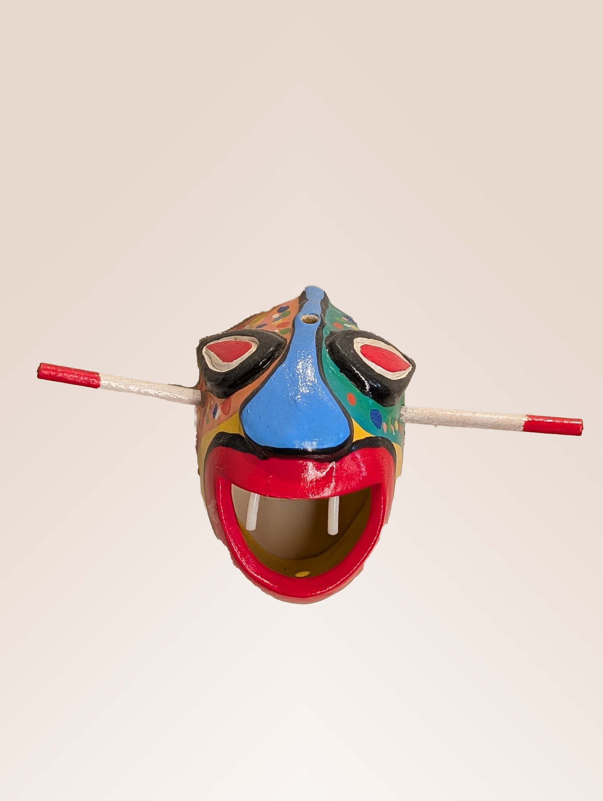 Colorful mask with red mouth and eyes, blue nose, and two sticks.