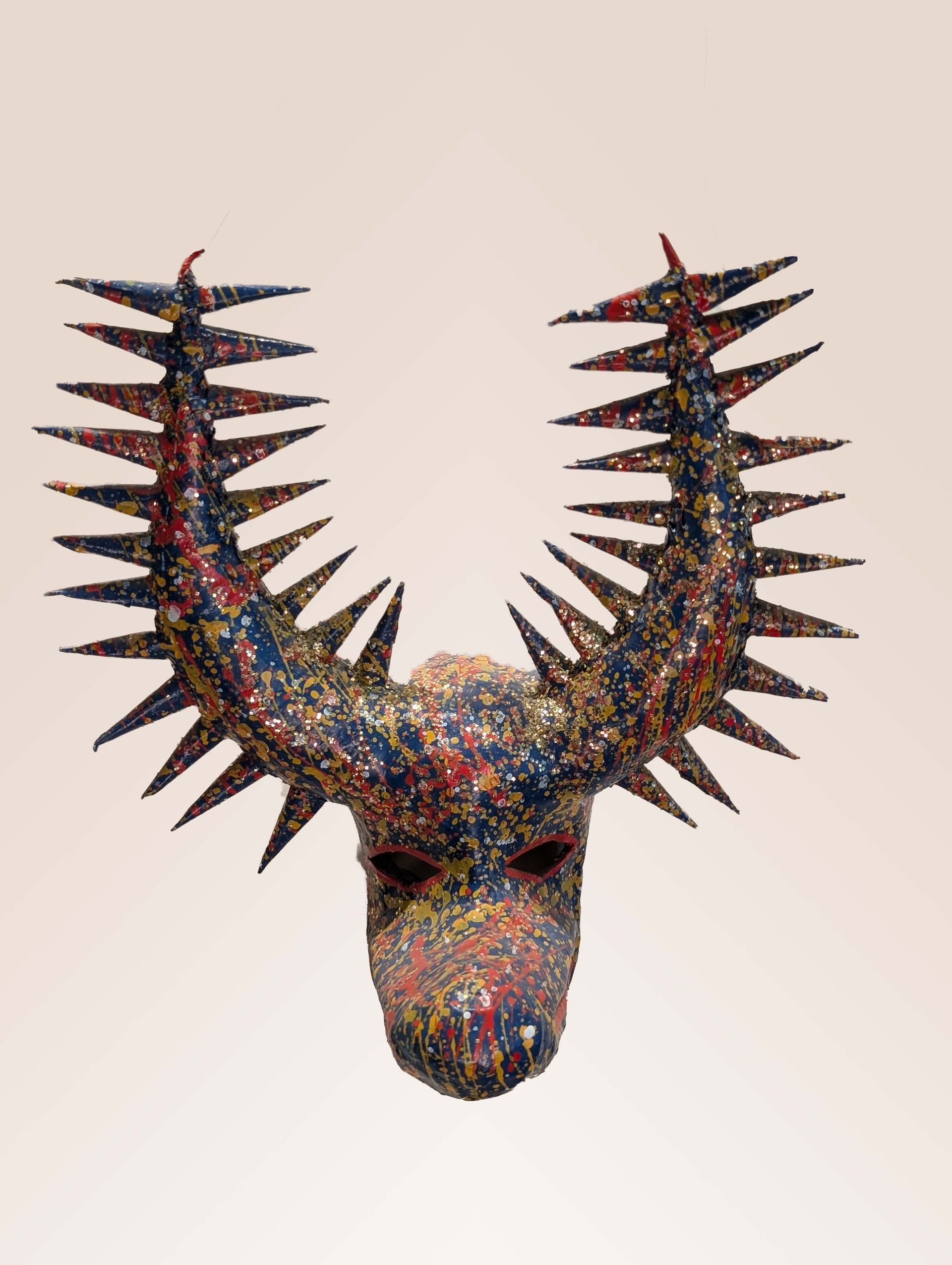 Mask of a horned creature with sharp spikes. Multi-colored with red, blue, and yellow.