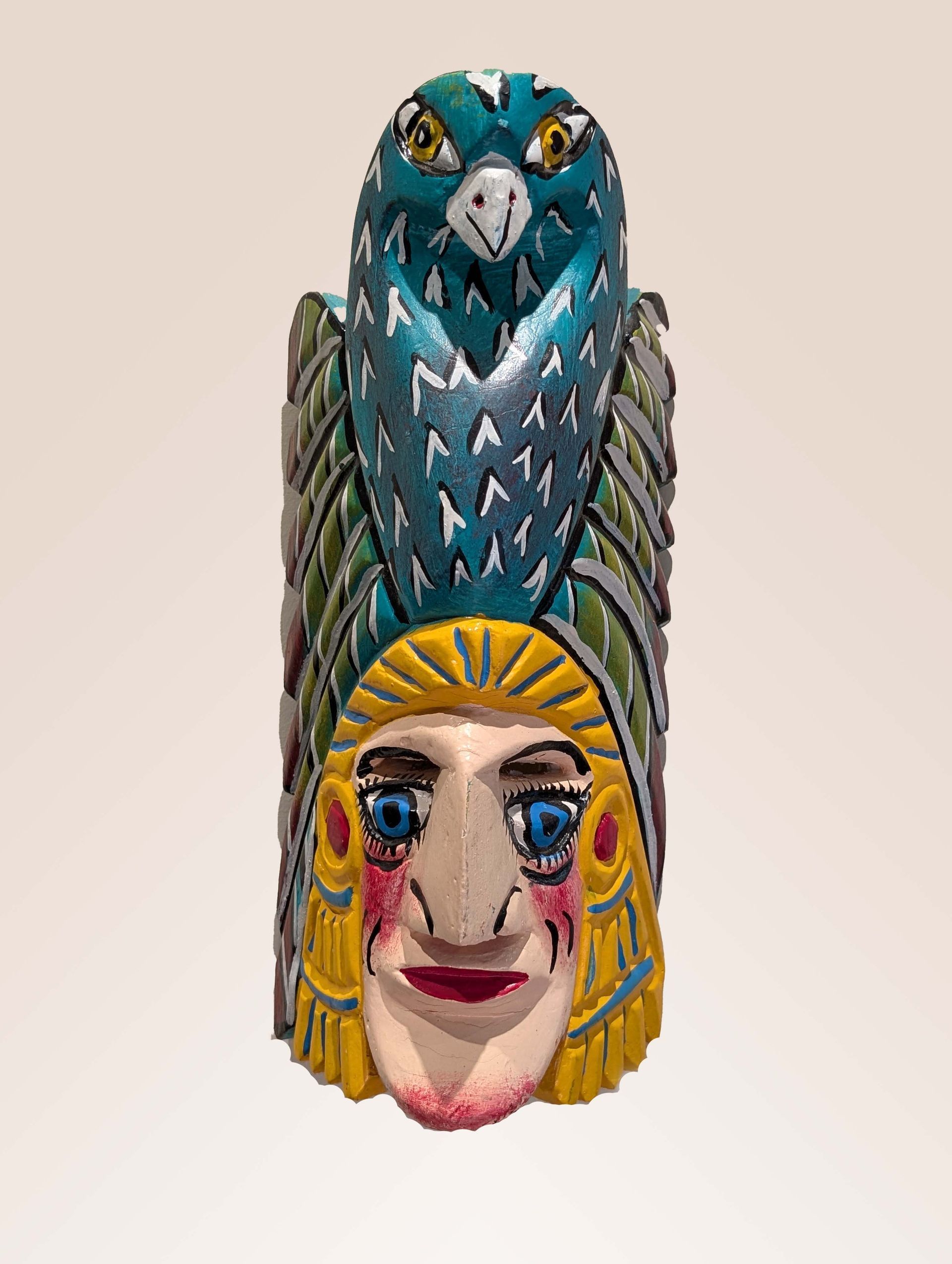 Carved wooden sculpture: blue owl atop a human face with yellow headdress, colorful details.
